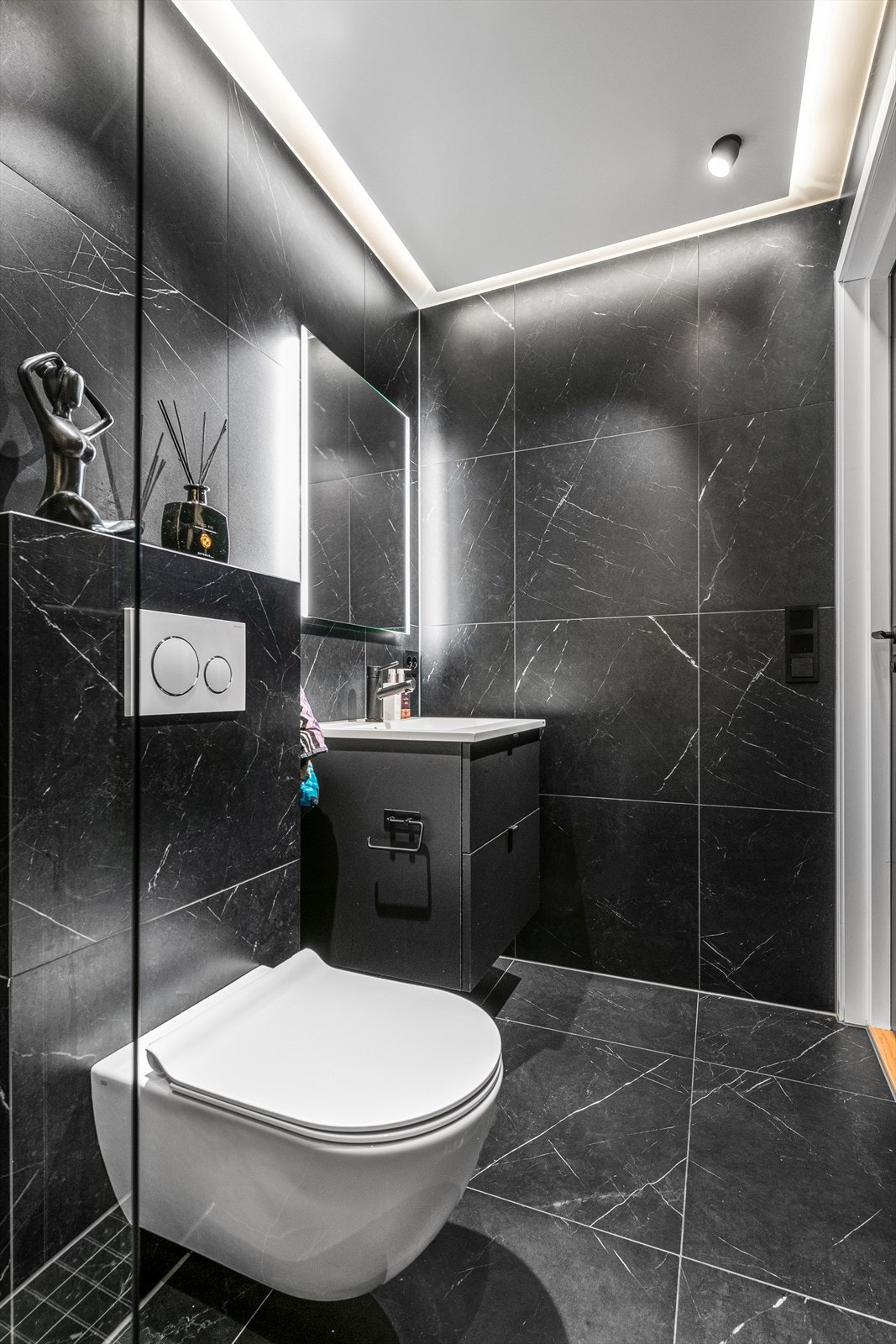 Badet i 1. etasje har sorte fliser på gulv og vegger, sort inneredning og speil med lys over servant Galleribilde