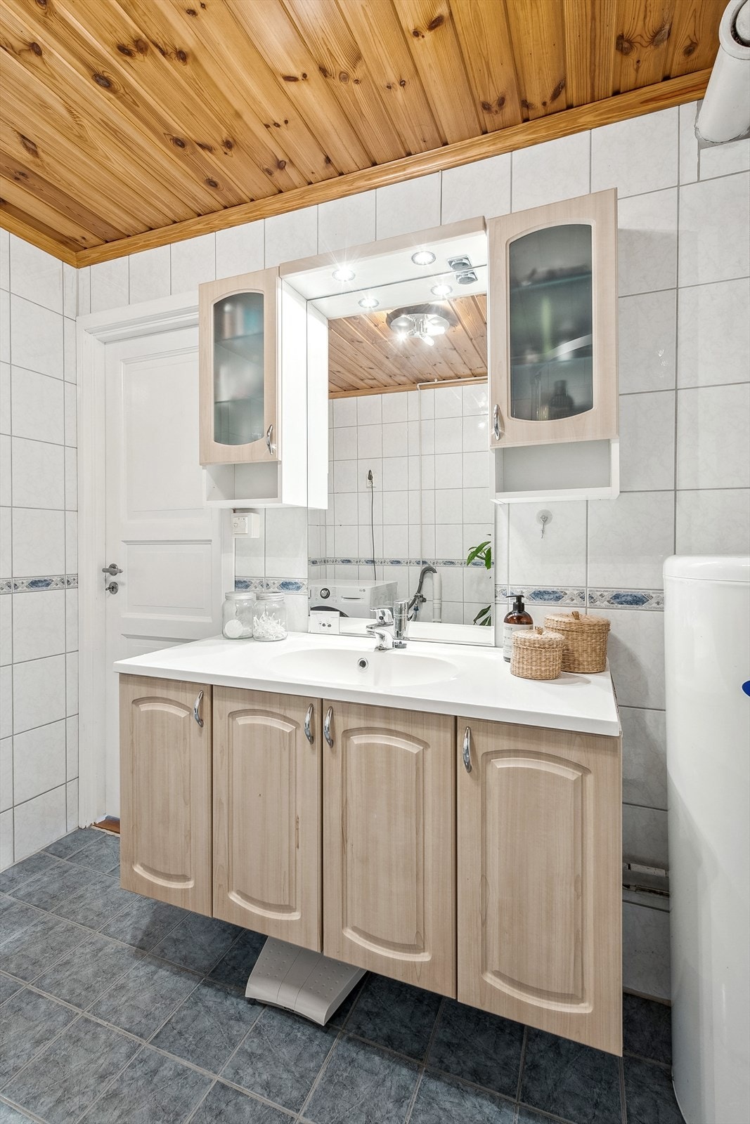 Badet består av fliser på gulv og vegger. Stor heldekkende servant på underskap. Speil med skapsystemer rundt. Galleribilde