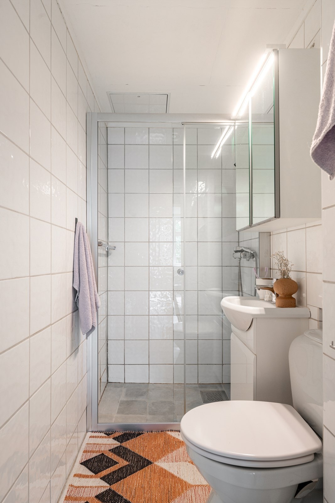 Innredningen består av et underskap/overskap, servant, speil, lys, gulvmontert toalett og dusjsone med skyvedør. Galleribilde