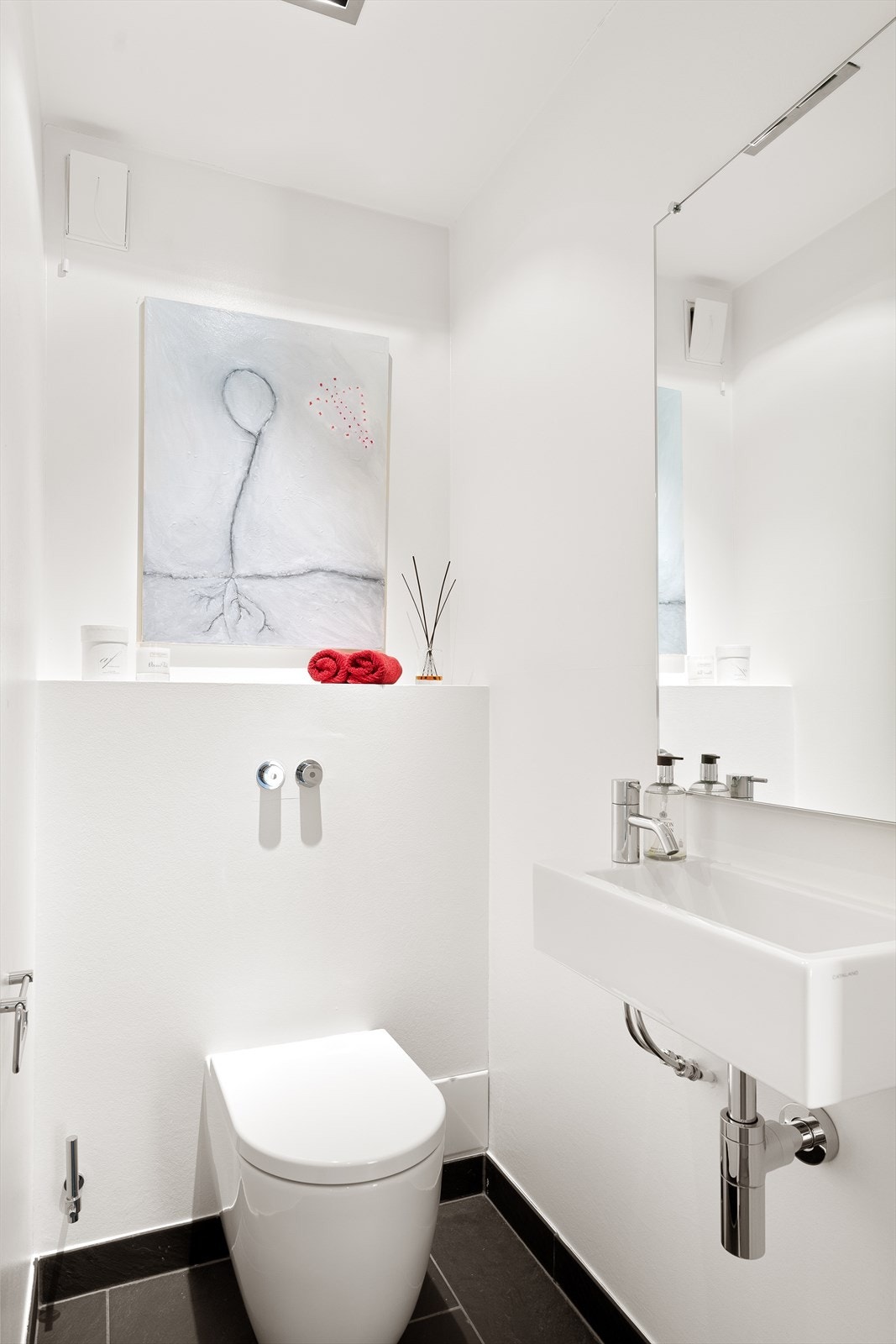 Separat toalettrom med flislagt gulv, malte gipsplater på vegg og tak med innfelte downlights. Toalettrommet er innredet med vegghengt servant med armatur og trykknapper toalett fra Vola med innebygget sisterne. Galleribilde