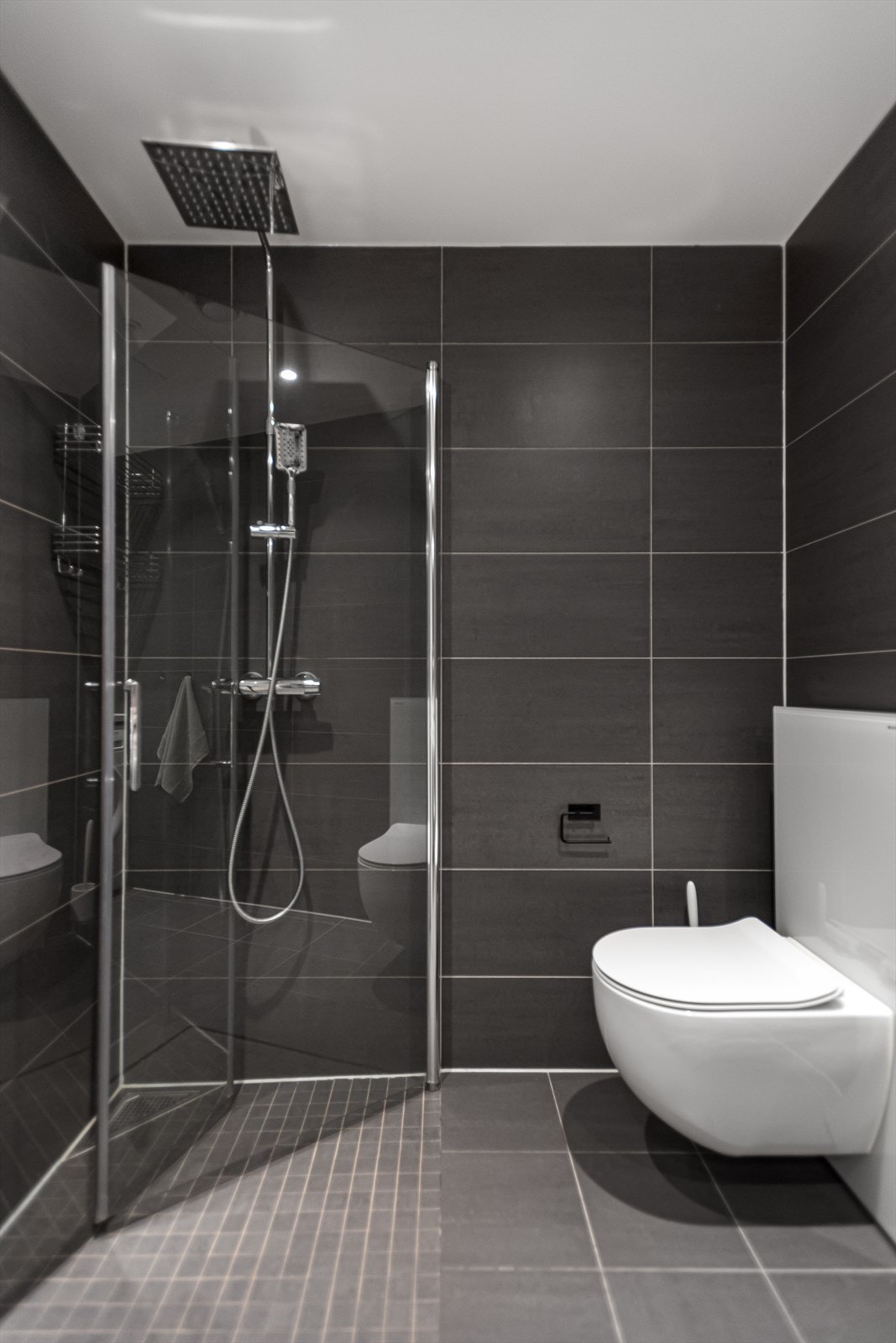 Rommet er innredet med dusj på gulv, veggfestet klosett samt servant med benkeskap. Galleribilde