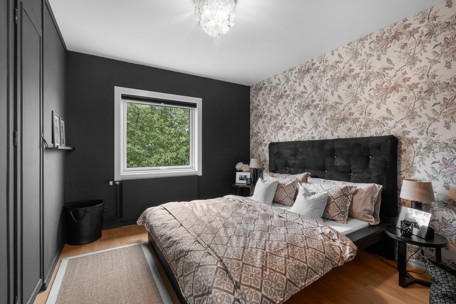 Leiligheten byr på to soverom av gode størrelser. Soverom nr. 1 har gulv av laminat og vegger malt i nøytrale farger, med en vakker kontrastvegg dekket med blomstret tapet som gir rommet et elegant preg. Galleribilde