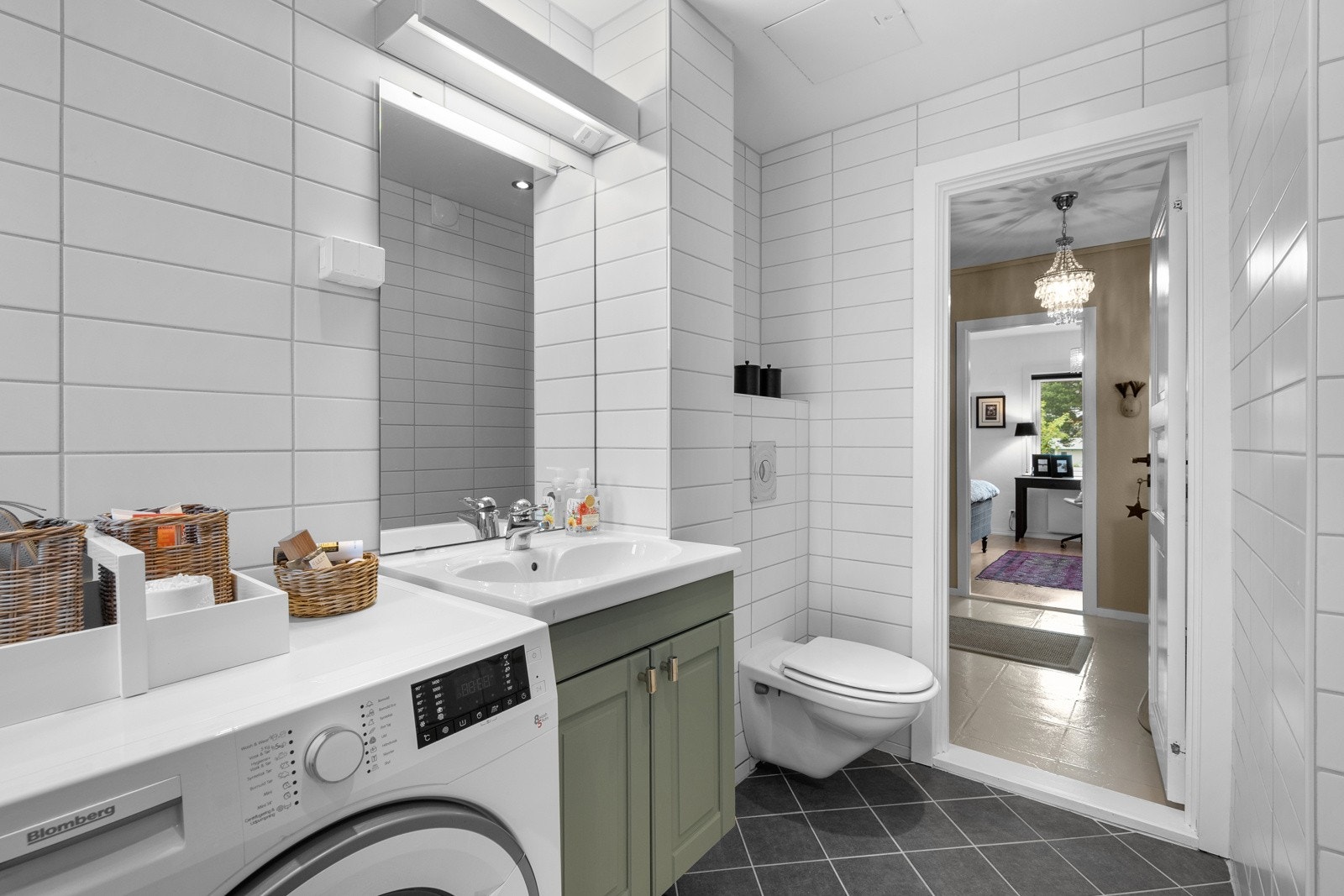 Badet er helflislagt med behagelig gulvvarme og er utstyrt med med en praktisk dusjnisje med glassvegger, vegghengt toalettt, servant med innredning og speil, samt opplegg for vaskemaskin. Galleribilde