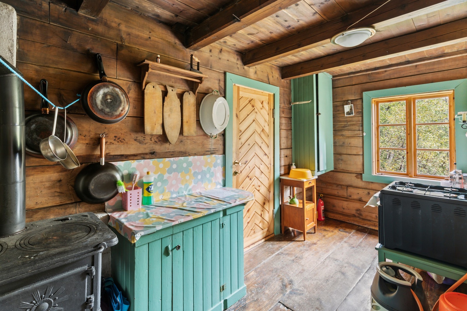 Kjøkkenet har montert en enkel, eldre innredning med benkeskap og hyller Galleribilde