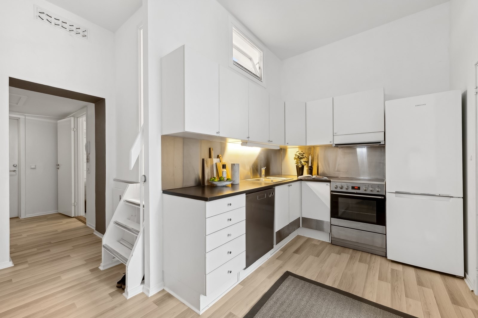 Videre inn i leiligheten finner man en åpen stue/kjøkkenløsning. Kjøkkenet har en moderne innredning med hvite glatte fronter. Galleribilde