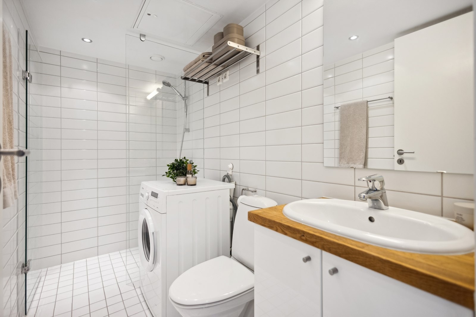 Delikat og tidløst bad innredet med toalett, dusjhjørne, servant nedfelt i eik benkeplate og speil med overlys. Galleribilde