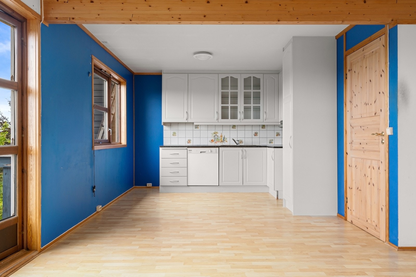 Klassisk kjøkken fra byggeår i åpen løsning mot stuen. Innredningen består av profilerte kremhvite fronter med foring opp til tak i kombinasjon med vitrineskap. Benkeplaten er laminert med nedfelt kum i rustfritt stål. Galleribilde