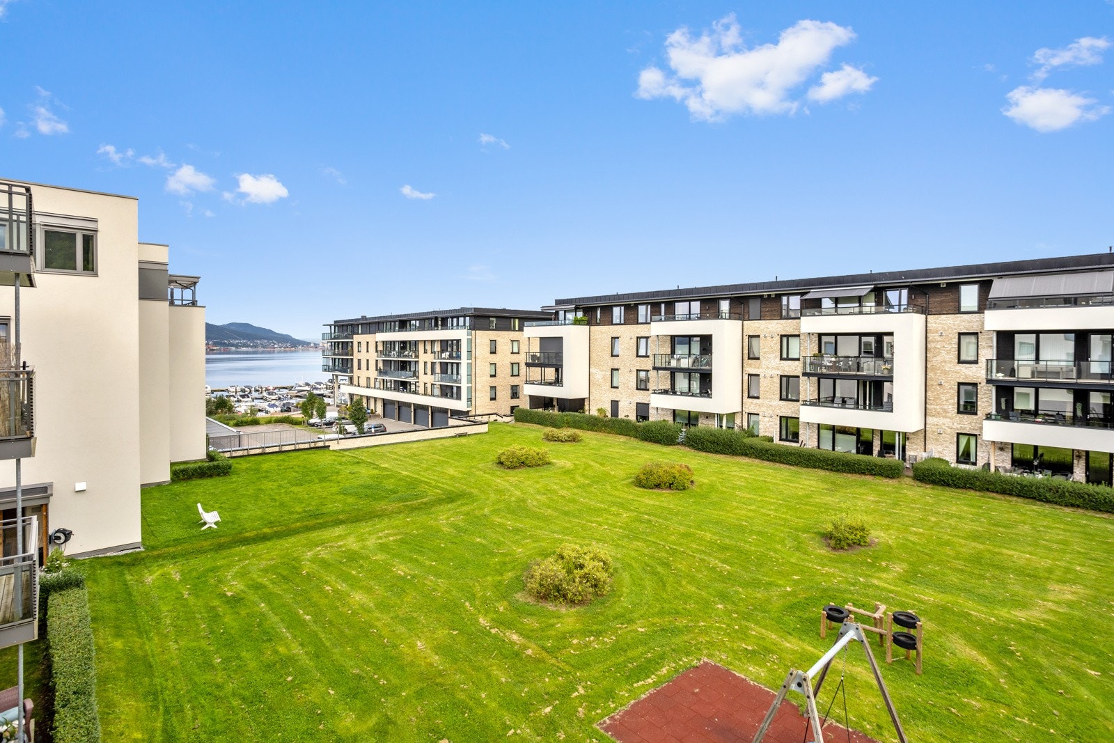 Fellesarealene mellom bebyggelsen er pent opparbeidet med grønne plener, hekker, trær og beplantninger Galleribilde