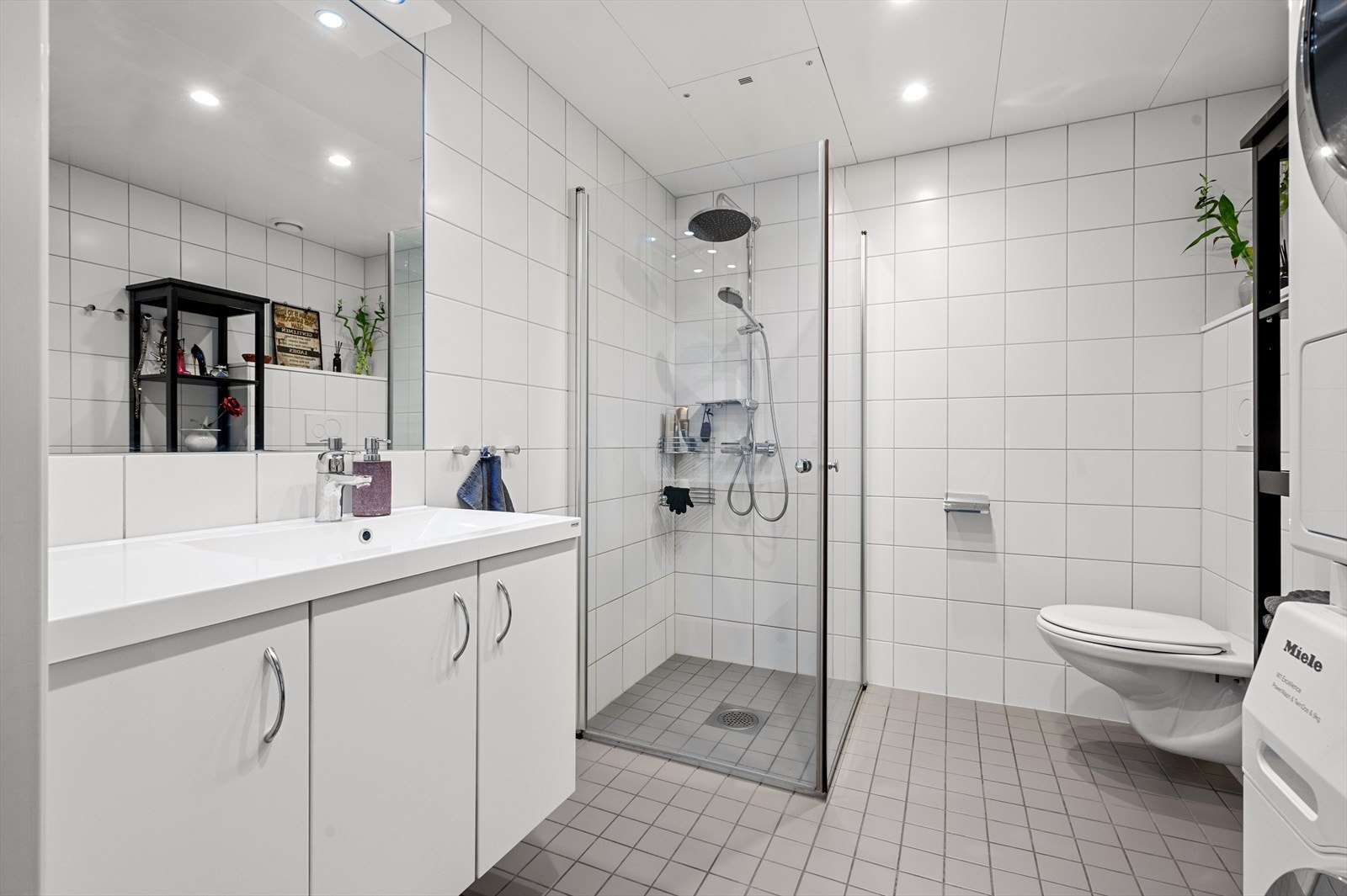 Romslig og moderne flislagt baderom med fine oppbevaringsløsninger. Galleribilde