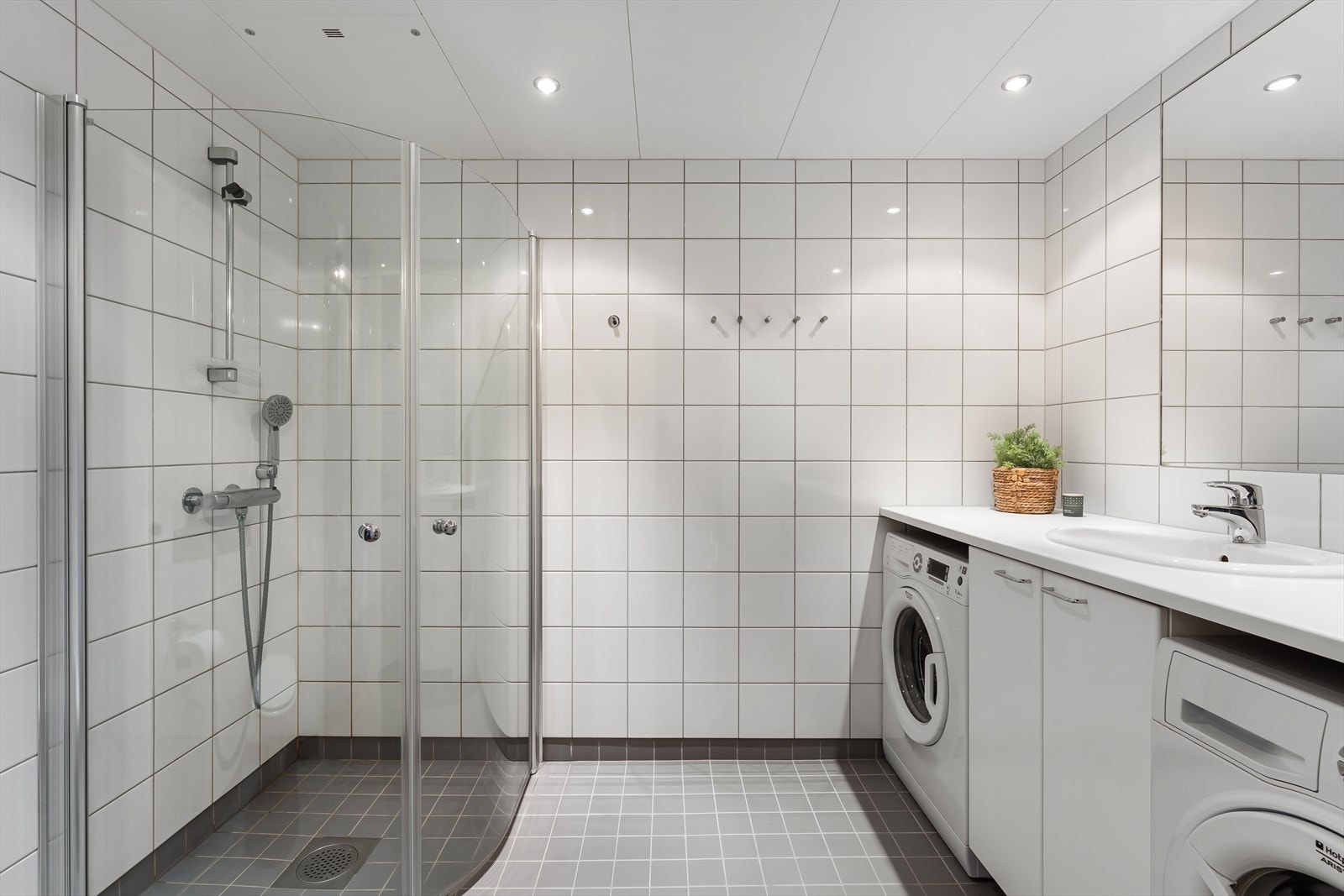Badet ligger inn fra entréen. Det har fliser på vegger og gulv. Dusjen har smarte dusjvegger som kan "foldes" inn. Innredning hvor både vaskemaskin og tørketrommel har fått sin plass. Servant med servantskap. Stort speil. Varmekabler i gulvet. Galleribilde