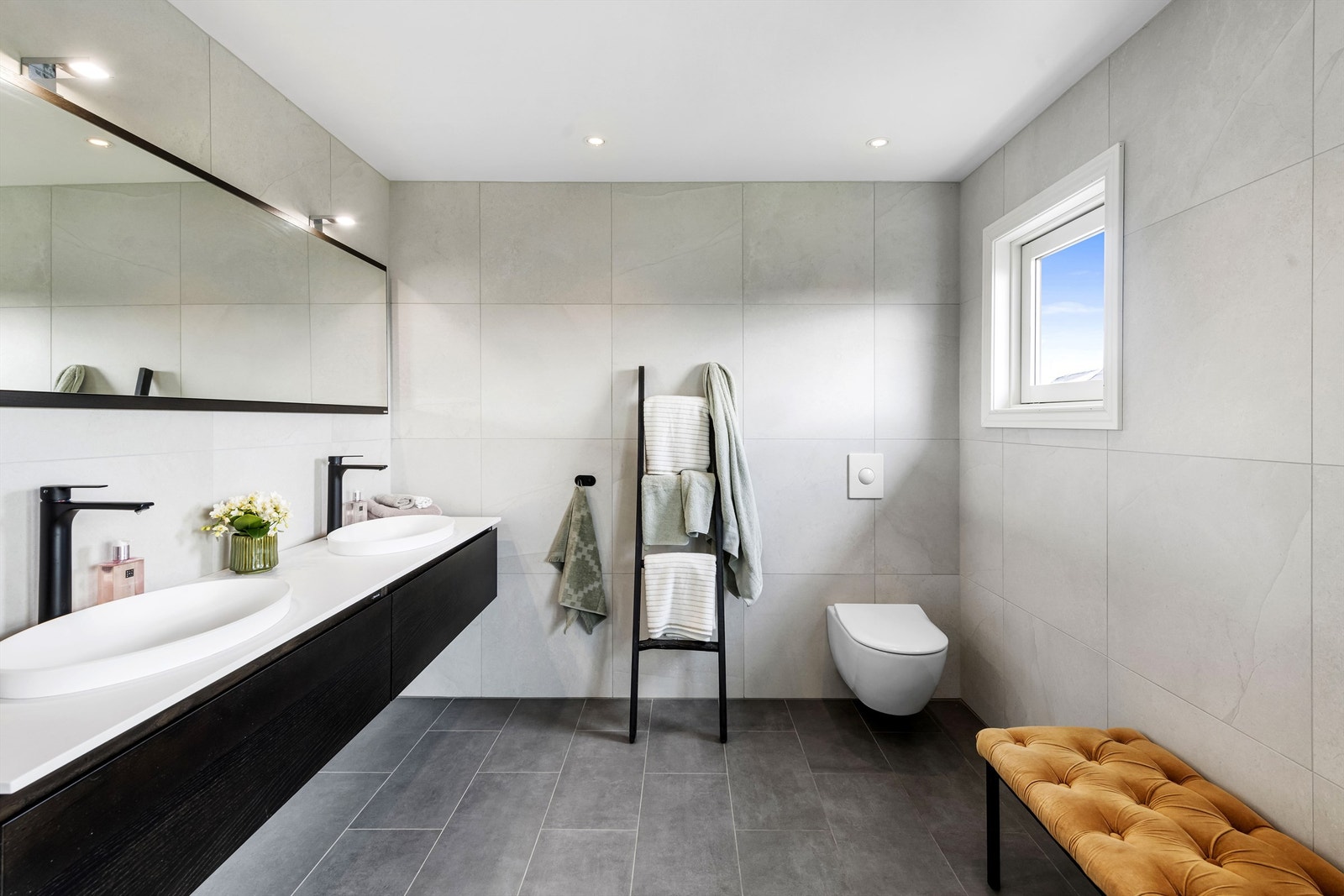 Badet i andre etasje er fra 2018 og har en familievennlig og lekker innredning. Her er det dobbelservant med sorte armaturer, på en hvit benk over sort skuffeseksjon i strømlinjeformet design, samt et bredt speil med belysning og et veggmontert toalett. Galleribilde