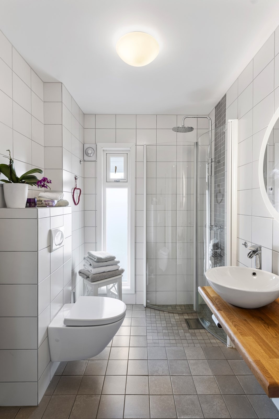 Badet i første etasje er fra 2014, og har en pen innredning med bolleservant på trebenk, rundt speil med belysning, et veggmontert toalett, og et dusjhjørne med innfellbare glassvegger, regnfallsdusj og hånddusj. Rommet har grå fliser på gulv med gulvvarm Galleribilde
