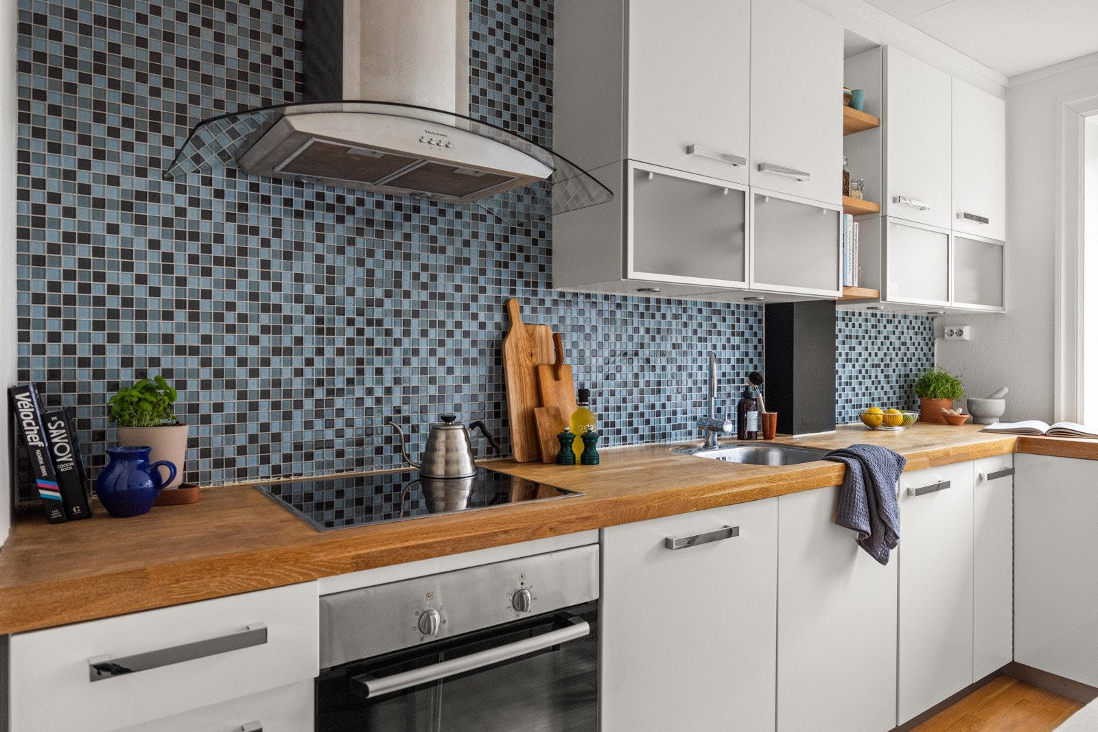 Moderne kjøkkeninnredning med hvite glatte fronter og laminat benkeplate med underlimt oppvaskkum. Mosaikkfliser mellom over- og underskap. Galleribilde