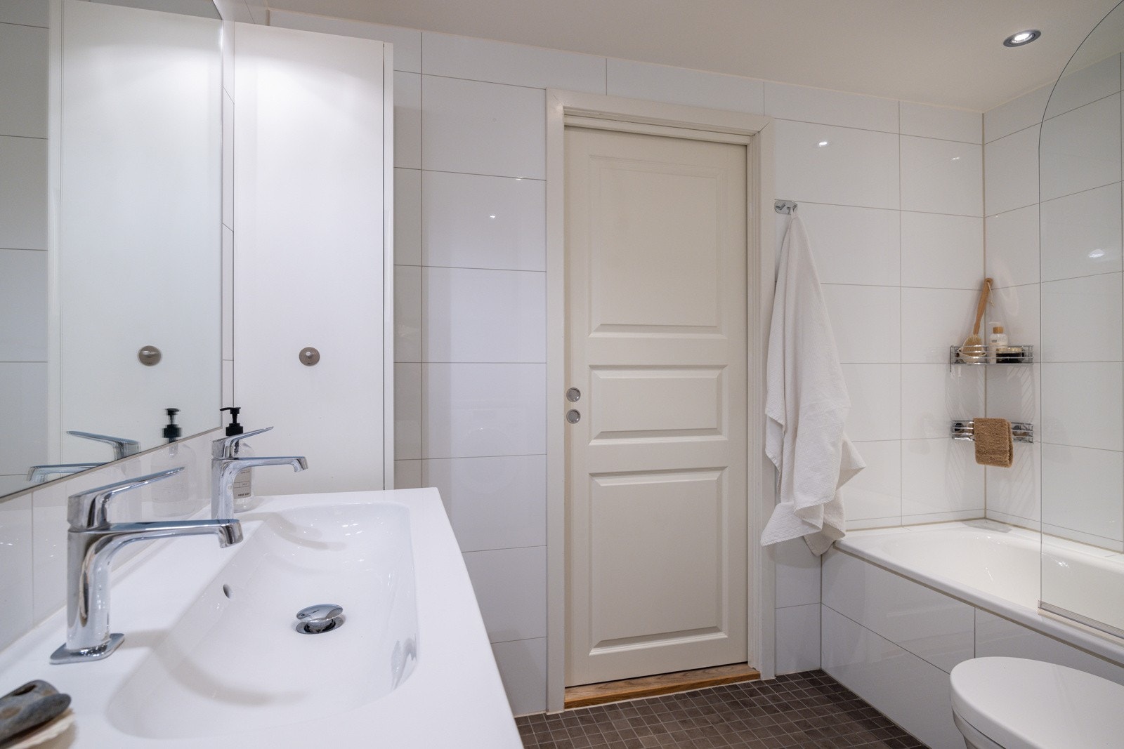 Lyst og moderne baderom med grå fliser på gulv med gulvvarme, hvite fliser på veggene og downlights i himlingen. Galleribilde