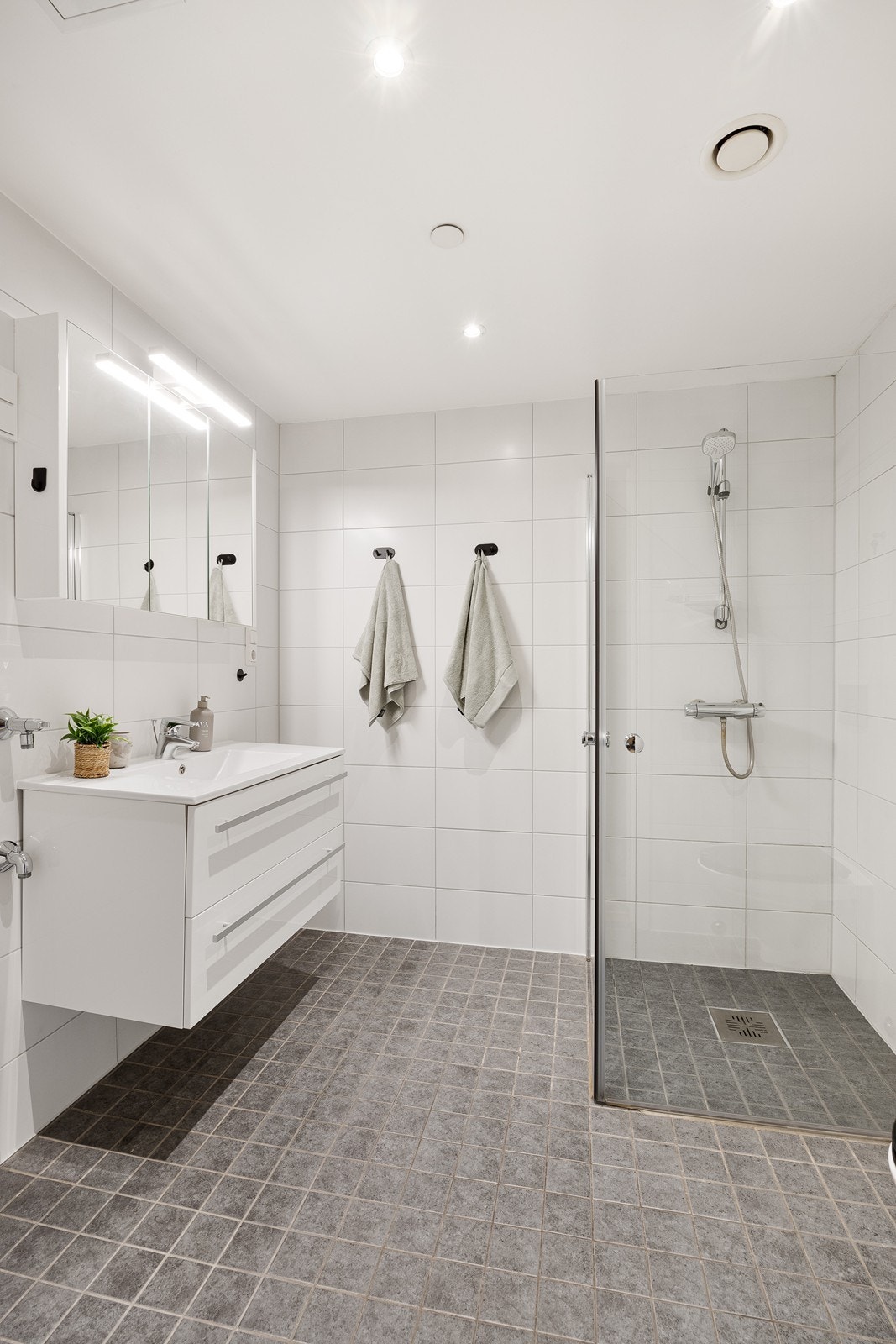 Innredet med heldekkende servant, speilskap med belysning, vegghengt toalett, dusjhjørne i glass og opplegg for vaskemaskin. Galleribilde