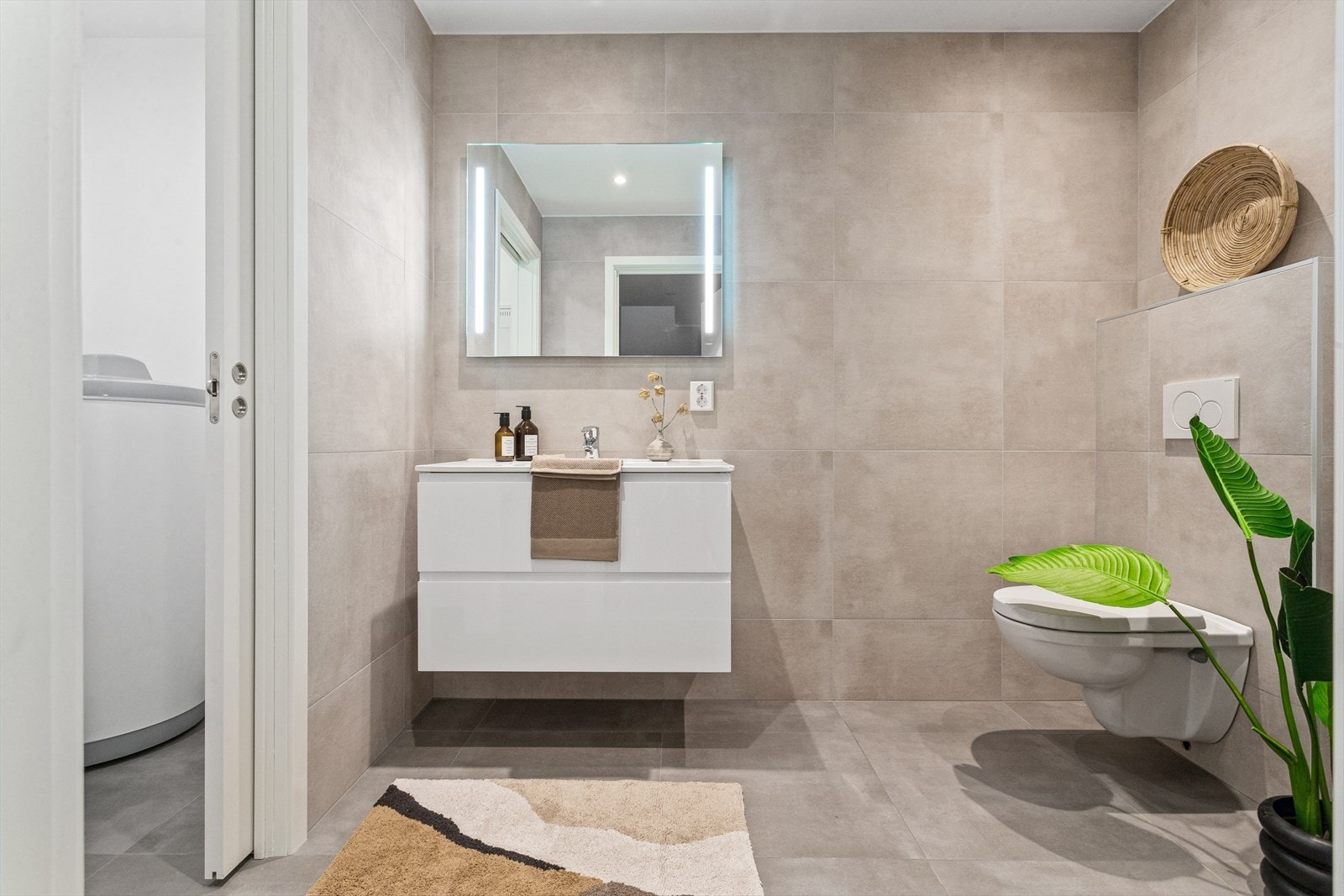 Badet er innredet med servant med skuffeseksjon, speil med belysning, vegghengt toalett og dusjnisje med med dusjdør. Galleribilde