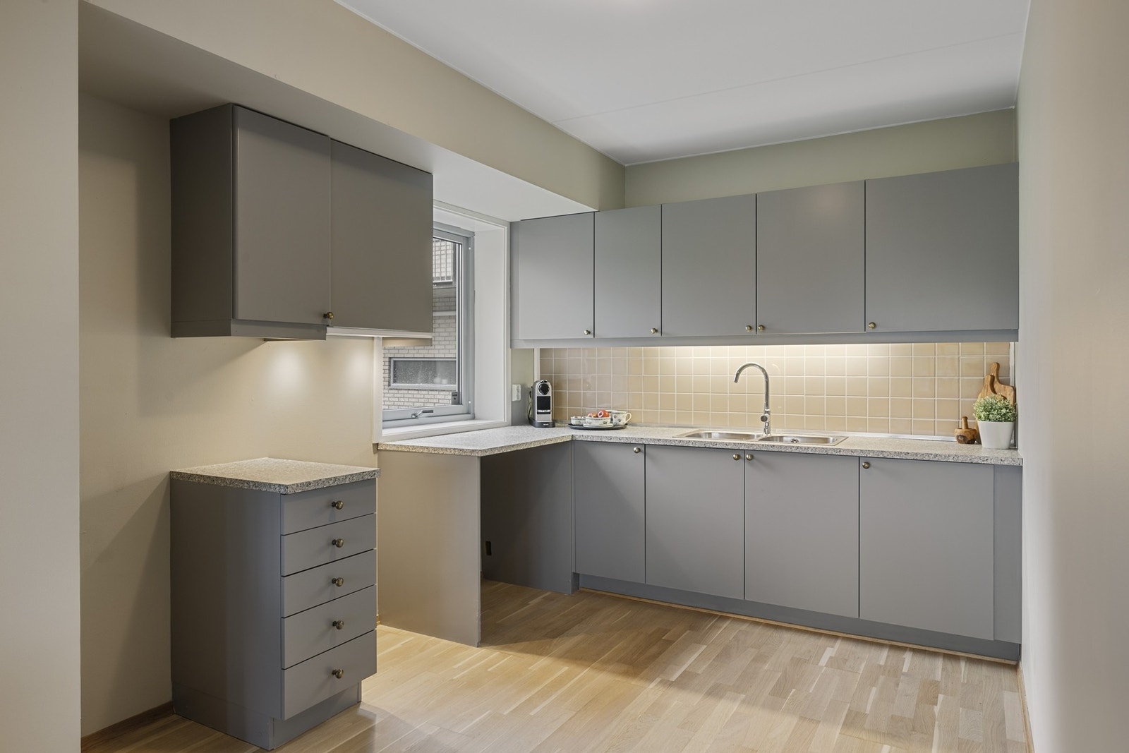 Pen kjøkkeninnredning med malte, slette fronter og laminert benkeplate, stålvask med skyllekum, avtrekksvifte over komfyrplass. Galleribilde