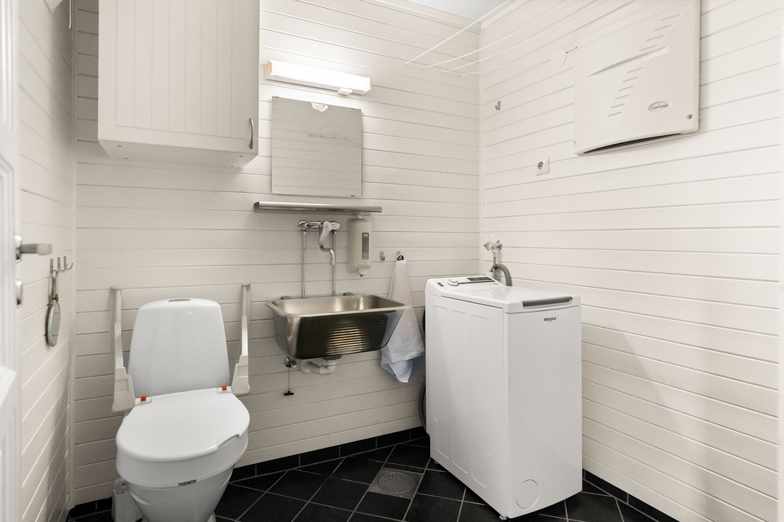 Det er inngang til et praktisk vaskerom, utstyrt med toalett, utslagsvask og opplegg for vaskemaskin. Galleribilde