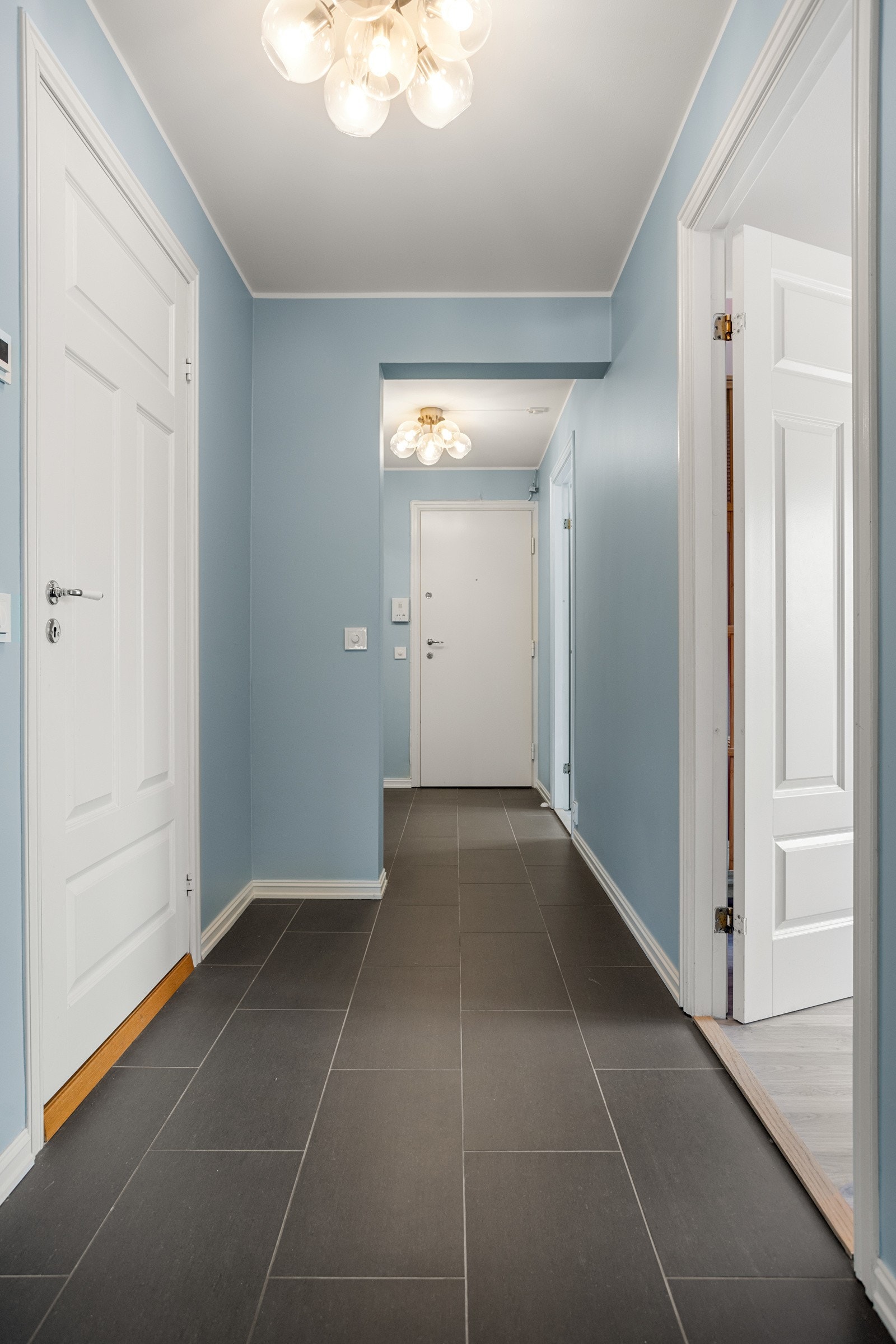 Leiligheten har en innbydende entré/gang med mørke fliser på gulvet og pent malte vegger Galleribilde