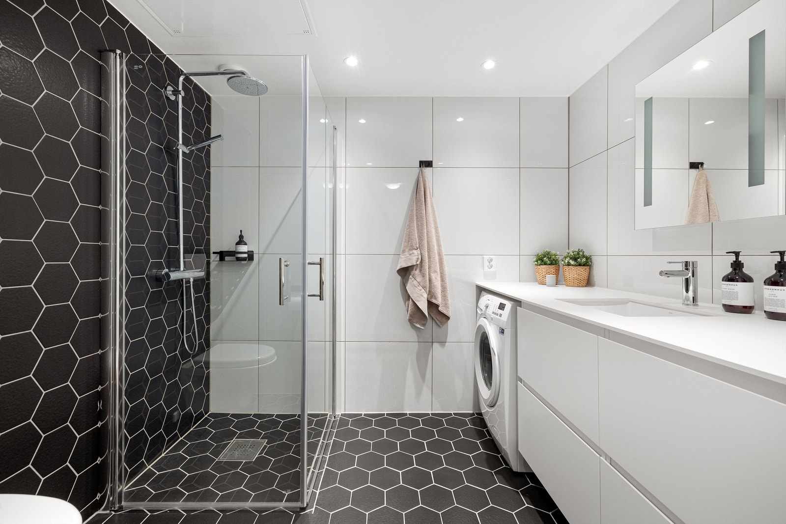 Innbydende bad på 5 m², innredet med baderomsmøbel med underskap, speil med integrert LED-lys, vegghengt WC med softclose og regnfallsdusj fra Grohe. Galleribilde