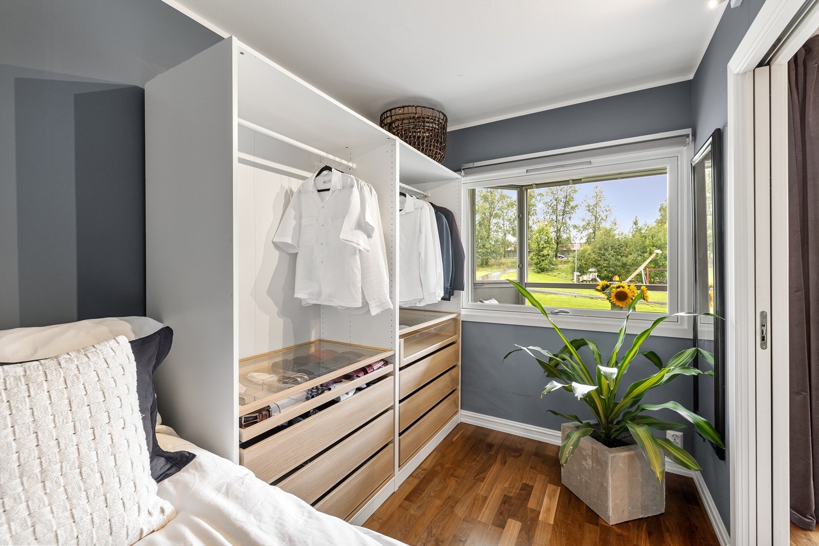 Rommet har nøttefarget parkett, malte vegger i en gråblå farge og åpen garderobe. Garderoben har hvite skapstammer med skuffer av foliert eik. Galleribilde