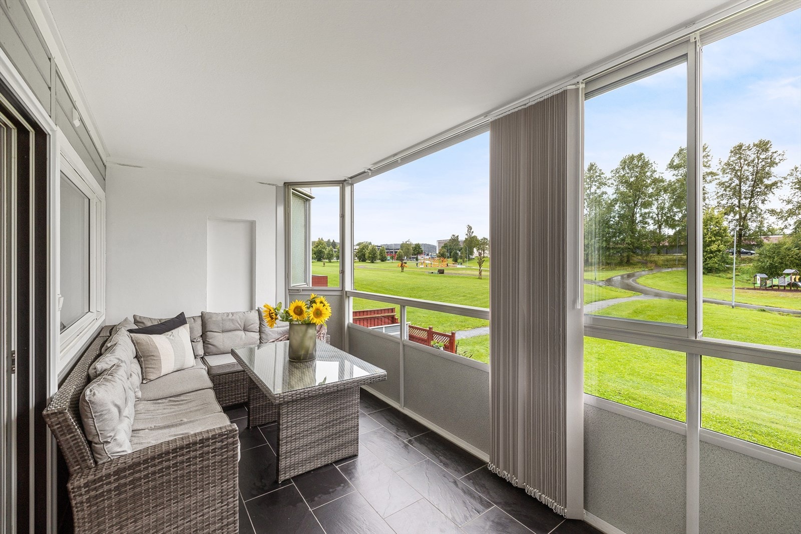 Balkongen har mørke fliser på gulvet, gråmalte panelvegger og pussede murvegger mot naboene. Galleribilde