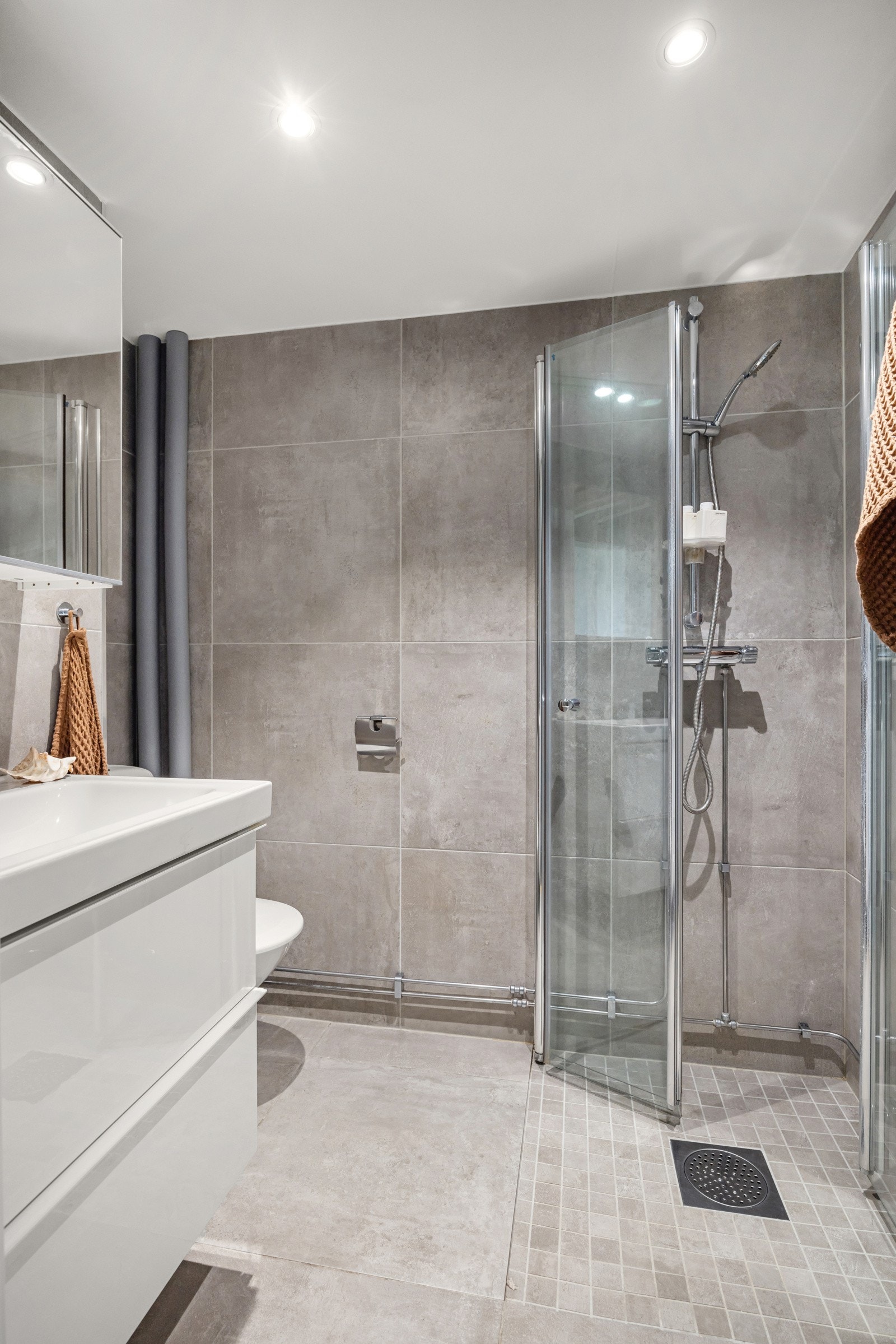 Fliser på gulv med gulvvarme, fliser på vegger og malt himling med downlights. I hjørnet av baderommet er det plass og opplegg for vaskemaskin. Galleribilde