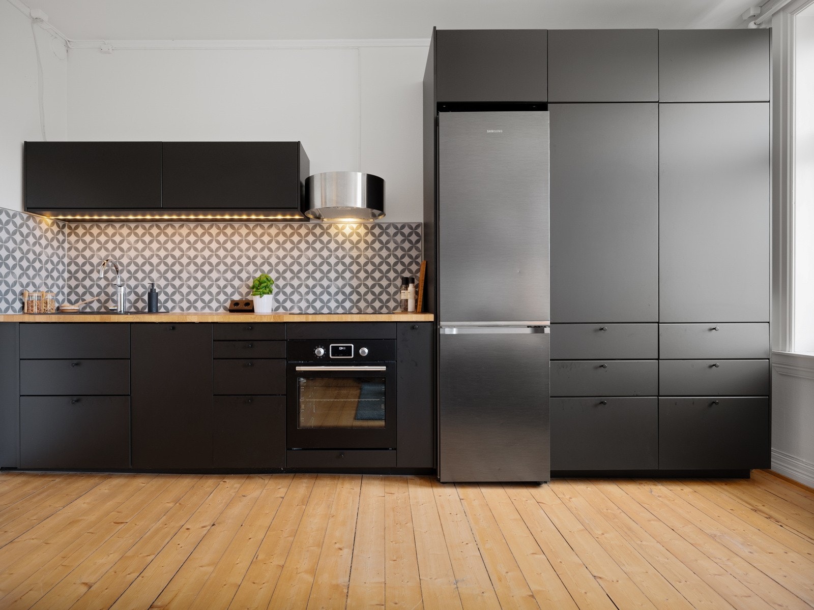 Innredningen har glatte fronter i grå-utførelse og benkeplate av tre. Under overskapene er det belysning og på benkeplaten er det stikkontakter. Galleribilde