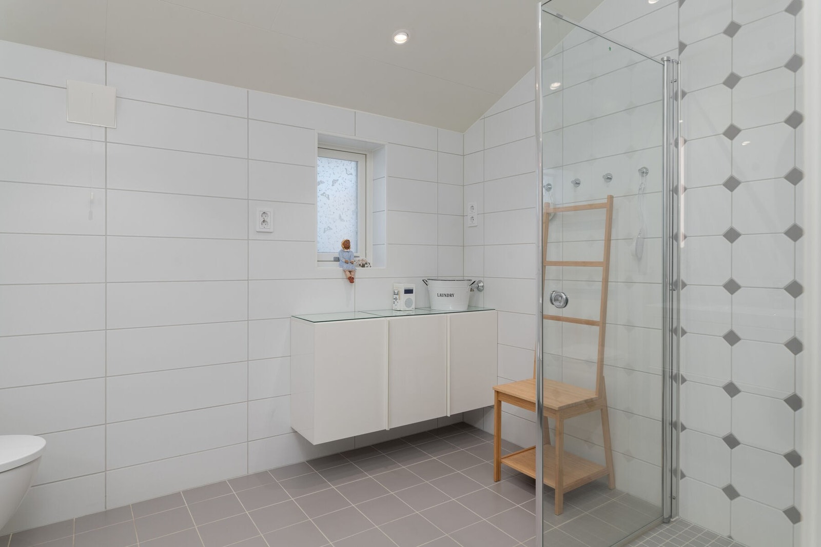 Badet har innredning med servant og speilskap, veggmontert toalett og dusjhjørne. Galleribilde