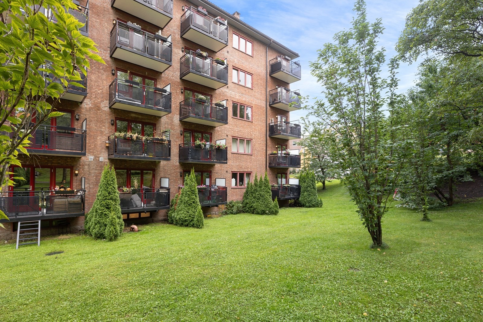 Pent opparbeidet fellesareal med diverse beplantning, trær, plenområder, sittebenker, sykkelparkering og asfalterte internveier. Galleribilde