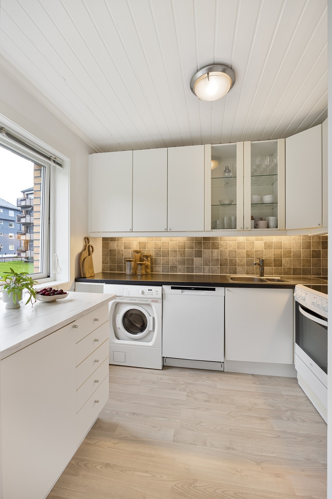 Innredningen har hvite, glatte fronter, vitrineskap og sort laminatbenkeplate med dobbel oppvaskkum. Galleribilde