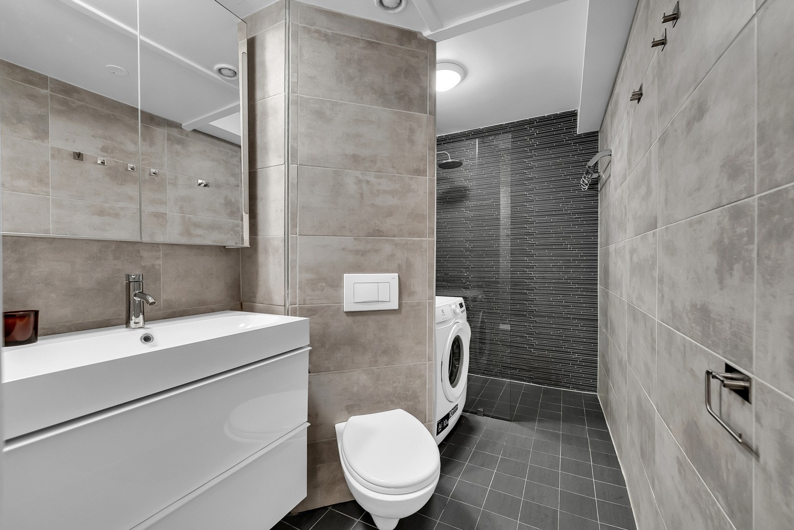 Badet i leiligheten ble pusset opp i 2014 med flis på flis og smøremembran i våtsoner. Badet har mørkegrå fliser på gulv og i dusjsone og veggene har lyser grå fliser. I gulvet er det varmekabler. Galleribilde