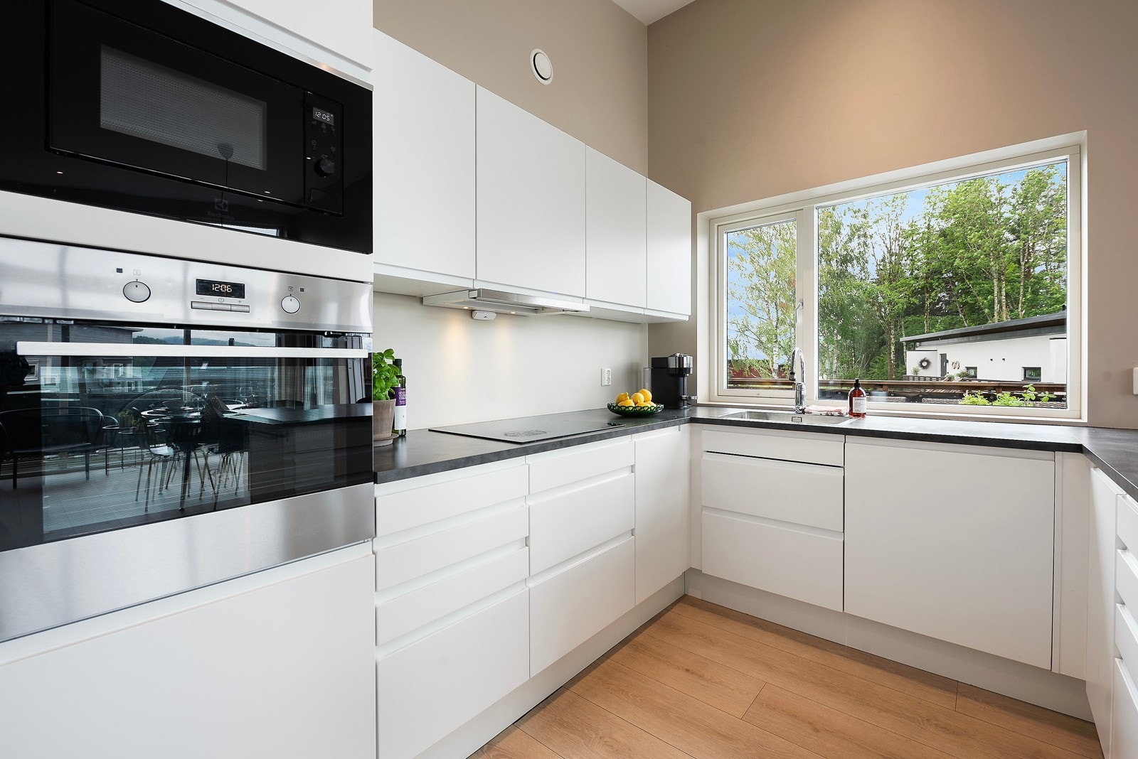 Kjøkkenet har stilrene, glatte fronter med gripekant, og benkeplate i mørk laminat. Vindu og downlights gjør sonen lys Galleribilde