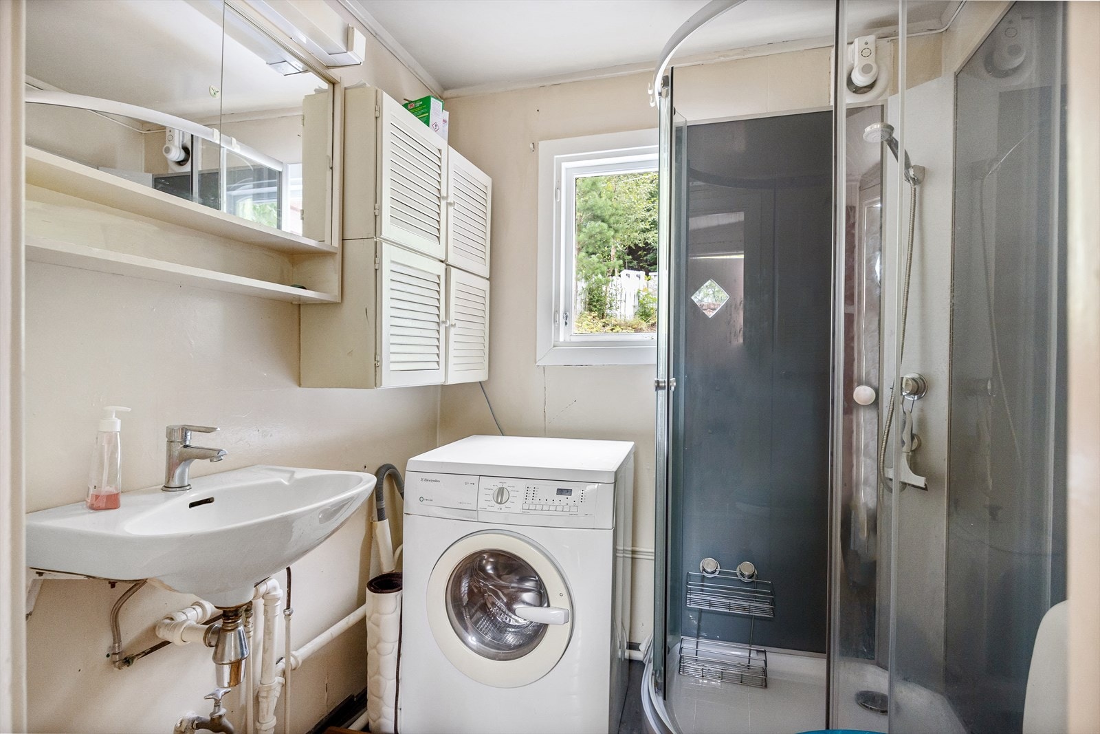 Badet er utstyrt med frittstående vannklosett, dusjkabinett, servant og speilskap. Galleribilde