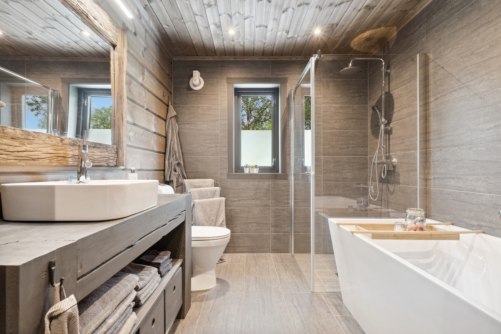 Badet er på 6 kvm og har flis på gulv samt flis/panel på vegger. Inneholder toalett, dusjhjørne med glassvegger, badekar og toppmontert vask på plassbygd innredning. Galleribilde