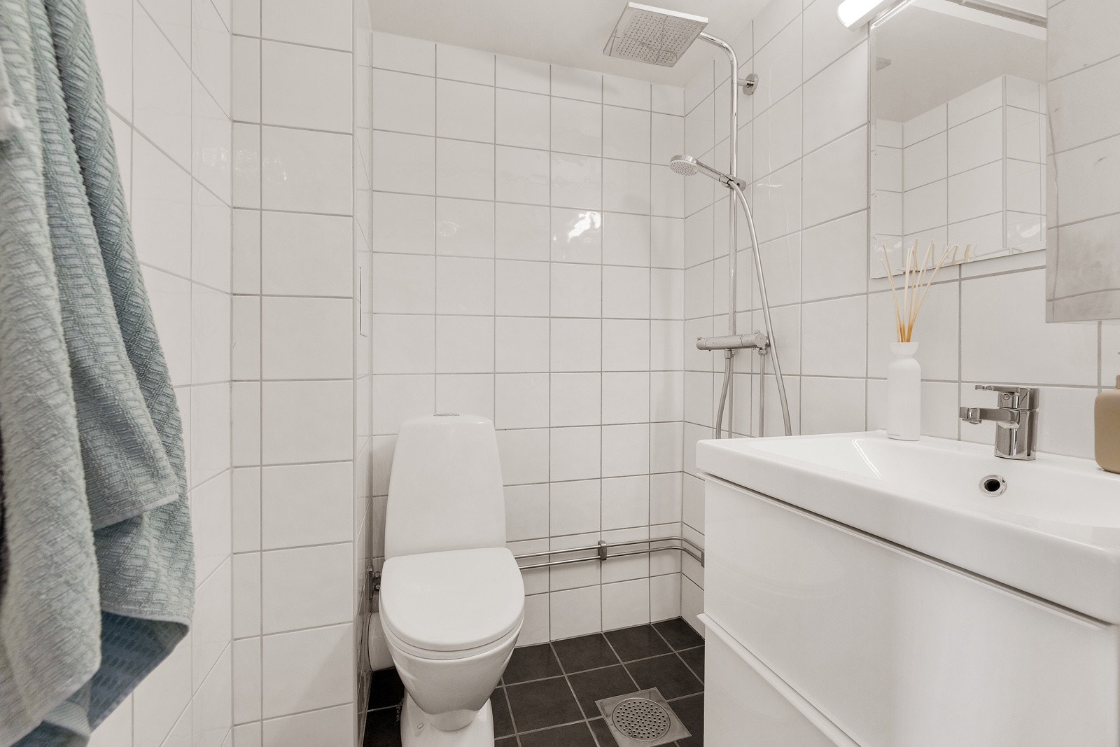 Innredningen på badet består av gulvstående toalett, servant med speilskap og dusjhjørne Galleribilde