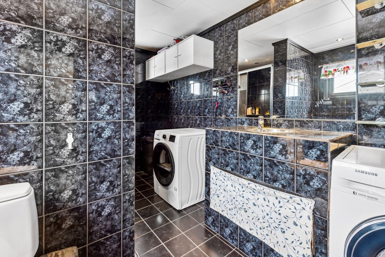 Baderom med mørke fliser på veggene og svarte fliser på gulvet. Galleribilde