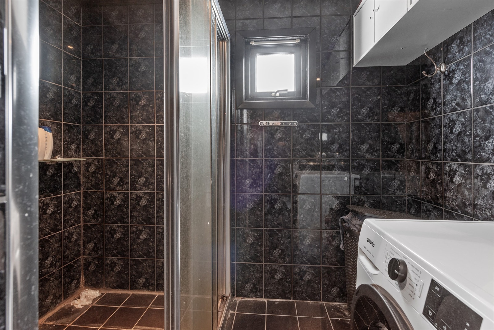 Baderommet er innredet med nedfelt servant i flislagt benk, innfliset speil, veggmonterte skap, gulvmontert toalett, dusjhjørne med vegger og opplegg for vaskemaskin. Galleribilde