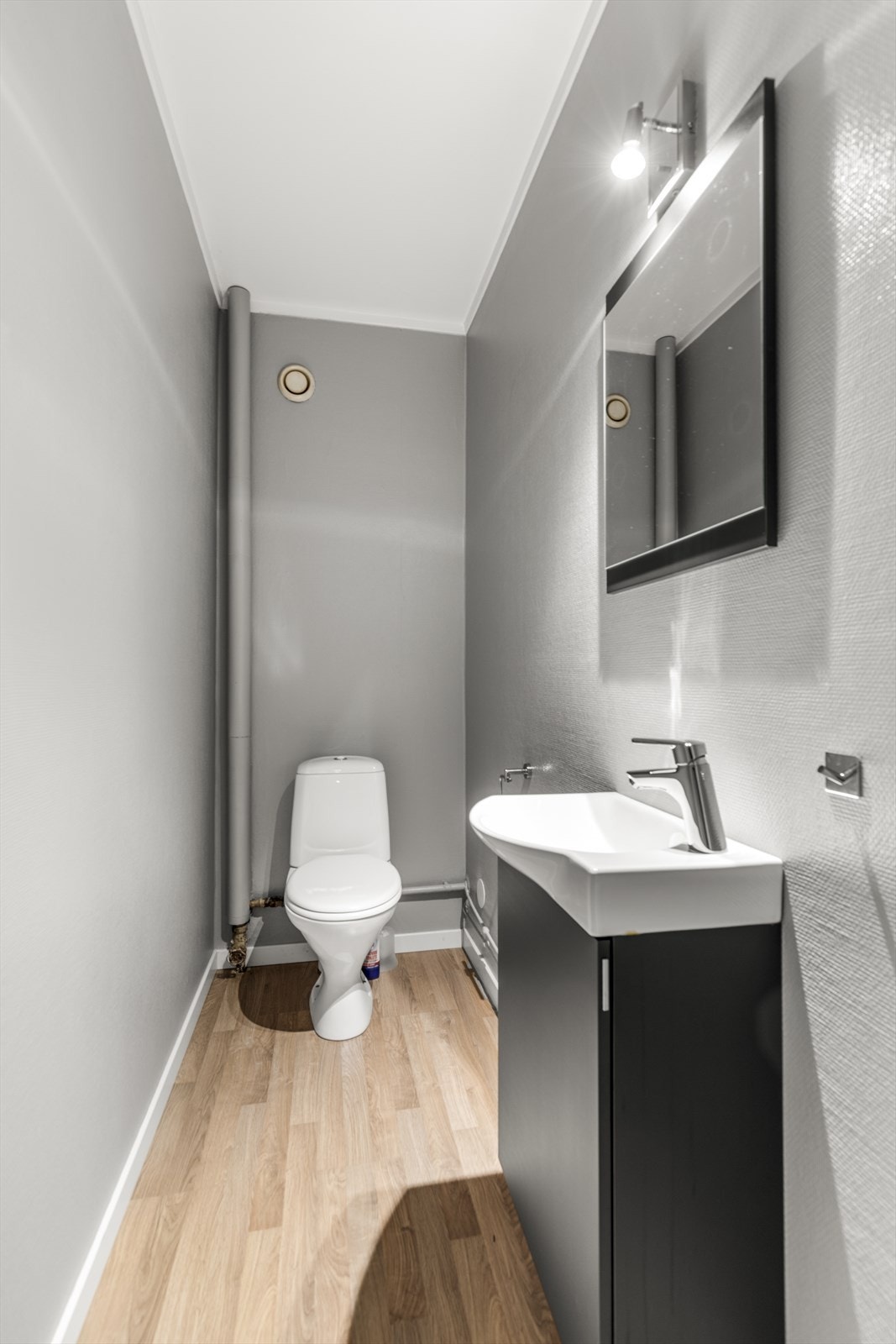 Eget toalettrom med et klosett, servant med underskap og speil med lys over. Galleribilde