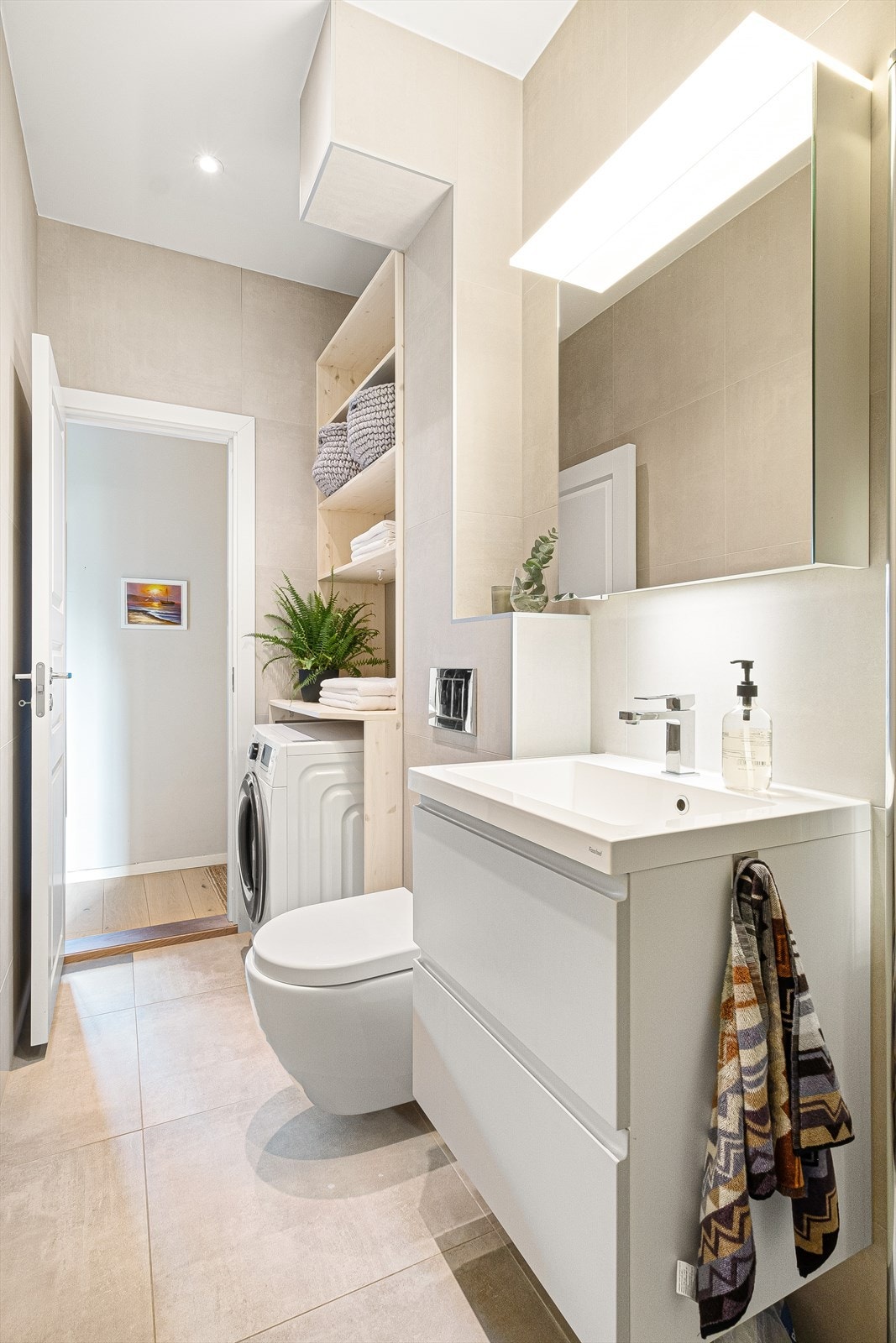 Badet er innredet med veggmontert wc, servant i innredning og speilskap med lys i rommet. Galleribilde