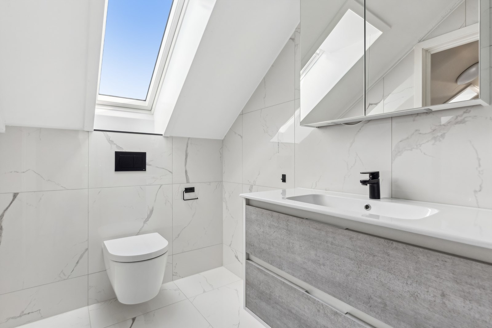 Innredet med vegghengt toalett, servant med speilskap, dusjhjørne og opplegg til vaskemaskin. Galleribilde