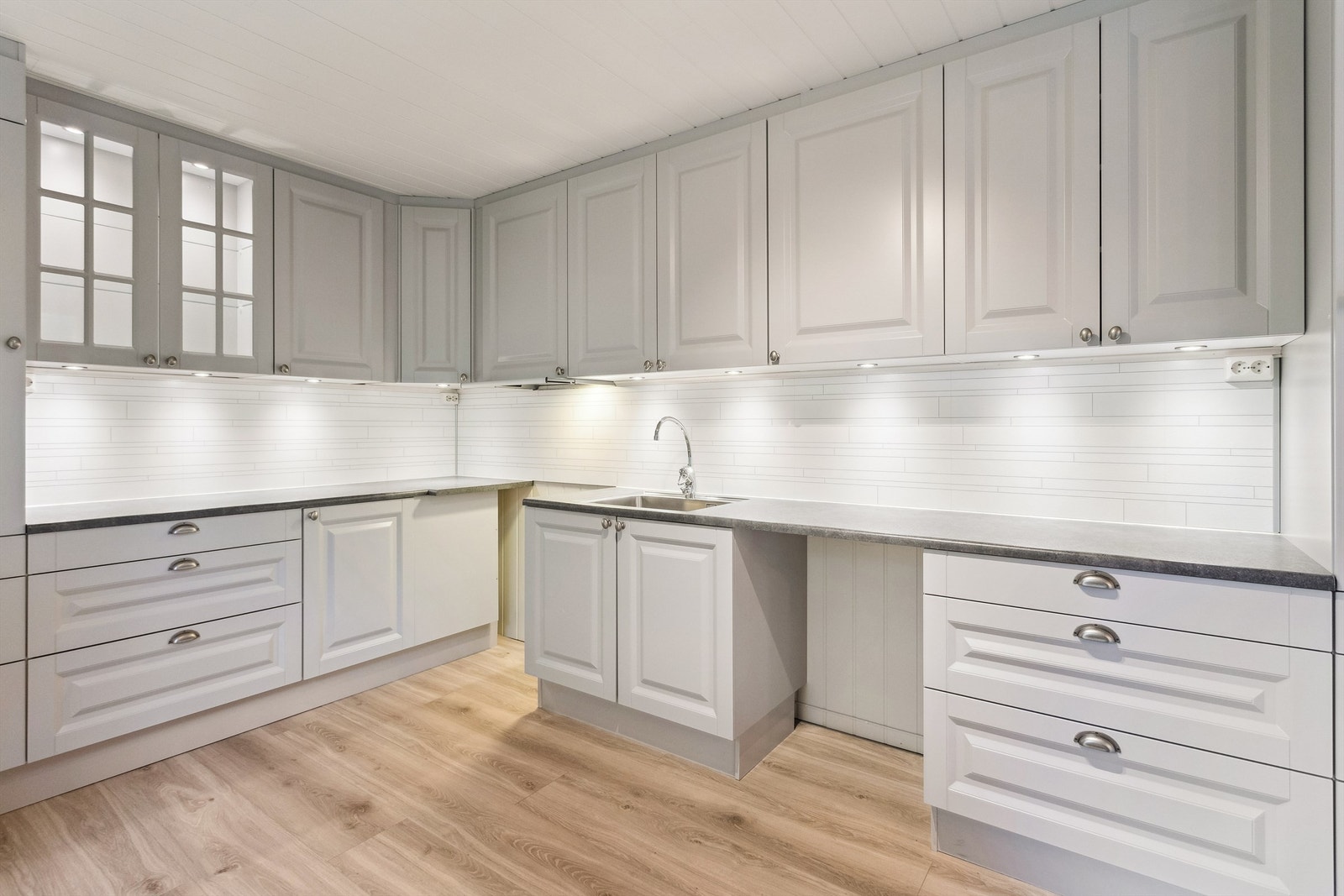 Innredningen består av skuffer, underskap, overskap og hæyskap. Ett overskap med glassdører. Hvite laminerte plater på veggflatene over kjøkkenbenker. Galleribilde