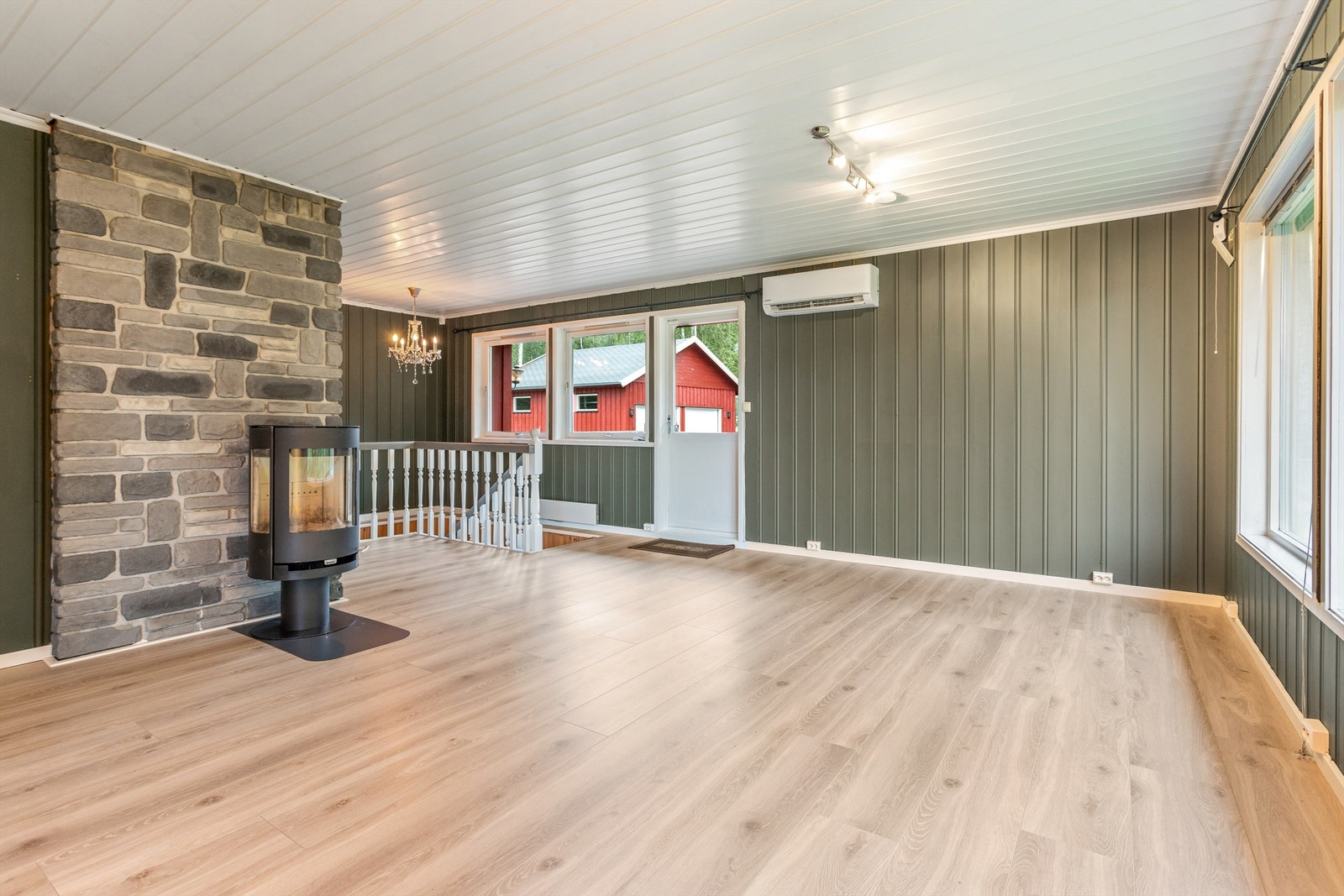 Her er det gode møbleringsmuligheter. Vedovn montert på svart plate mot steinlagt vegg og varmepumpe montert på veggen til høyre for terrassedøren. Galleribilde