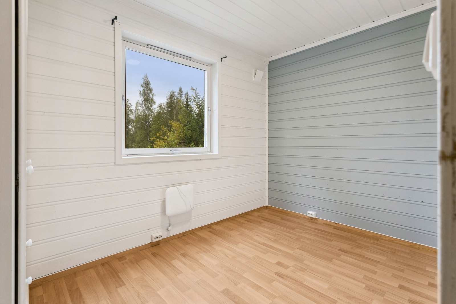 Det andre soverommet har hvitmalt panel på veggene, en kontrastvegg med lysgrå/blå malt panel og laminat på gulvet. Rommet er innredet med garderobeskap og panelovn montert på vegg. Galleribilde