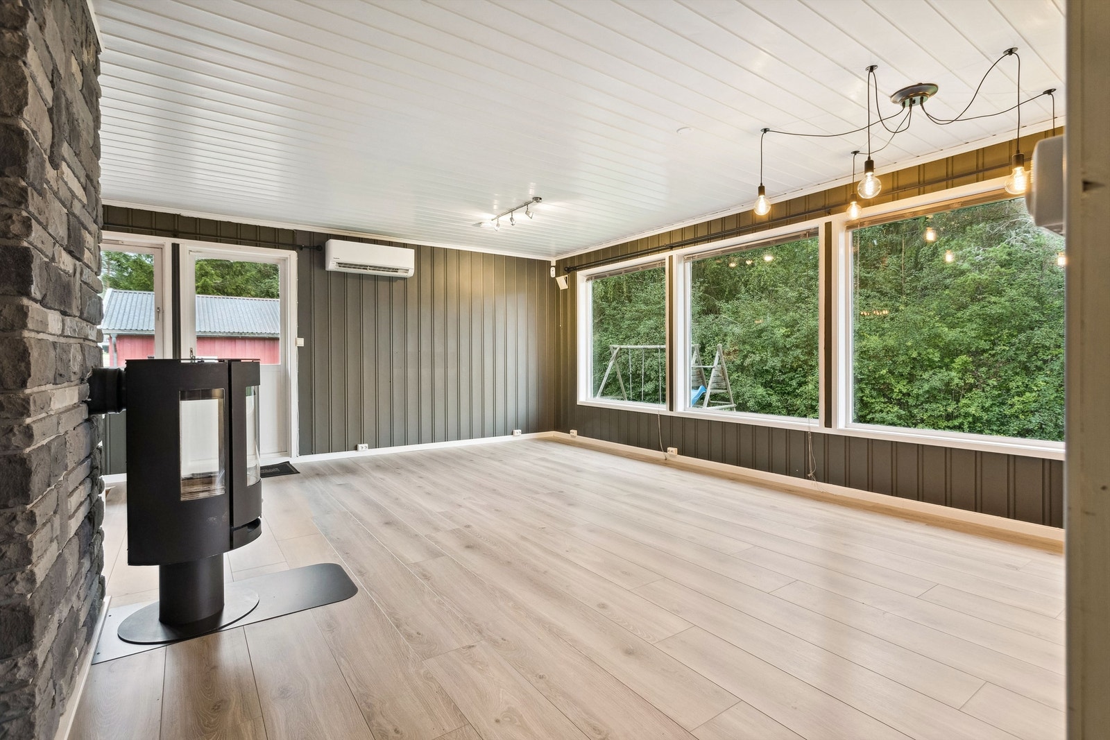 Stuen har grønnmalt stående panel på veggene og lys laminat på gulvet. Stuen er romslig med store vinduer som slipper dagslyset godt inn i rommet. Galleribilde