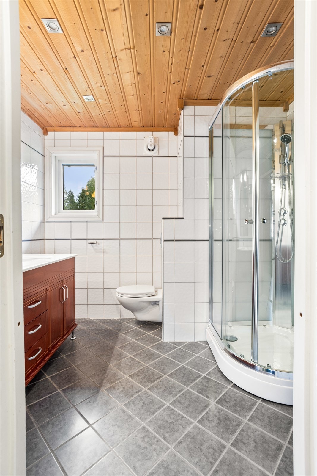 Flislagt baderom med grå fliser på gulvet og hvite fliser på veggflatene. Badet varmes opp med elektrisk gulvvarme. Galleribilde