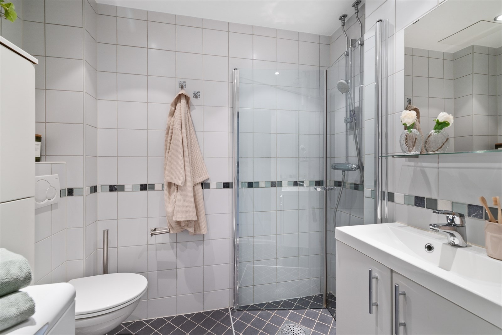 Badet er innredet med servantinnredning med hvite, glatte fronter, servant med ettgreps blandebatteri, vegghengt klosett, dusjdører, dusjamatur og det er opplegg og plass til vaskemaskin. Ventilasjon gjennom oppdriftsventil og tilluft fra spalte under dør Galleribilde