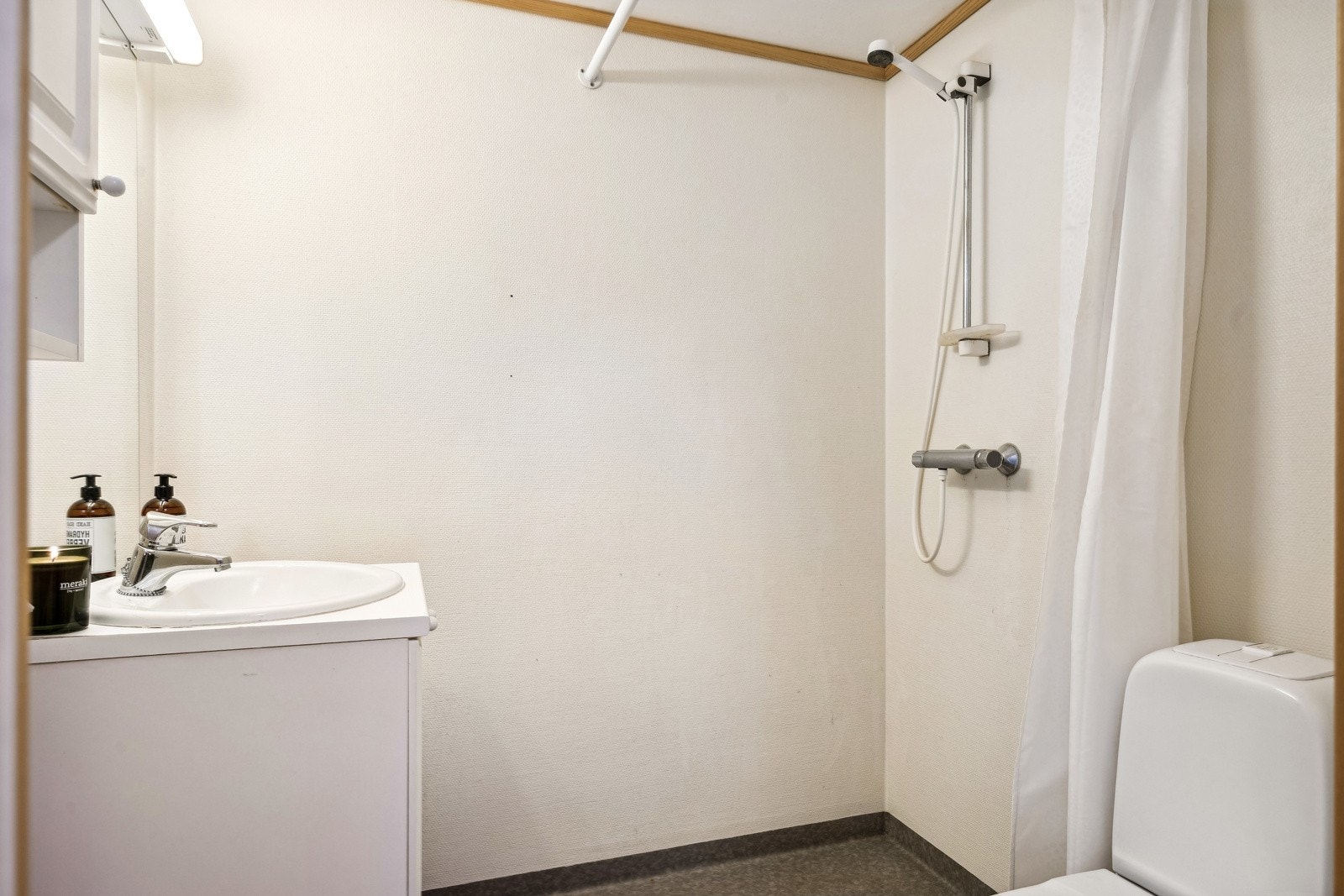 Lyst bad på hybelavd. med dusjgarnityr og servant i hvit innredning med speil og belysning. Galleribilde