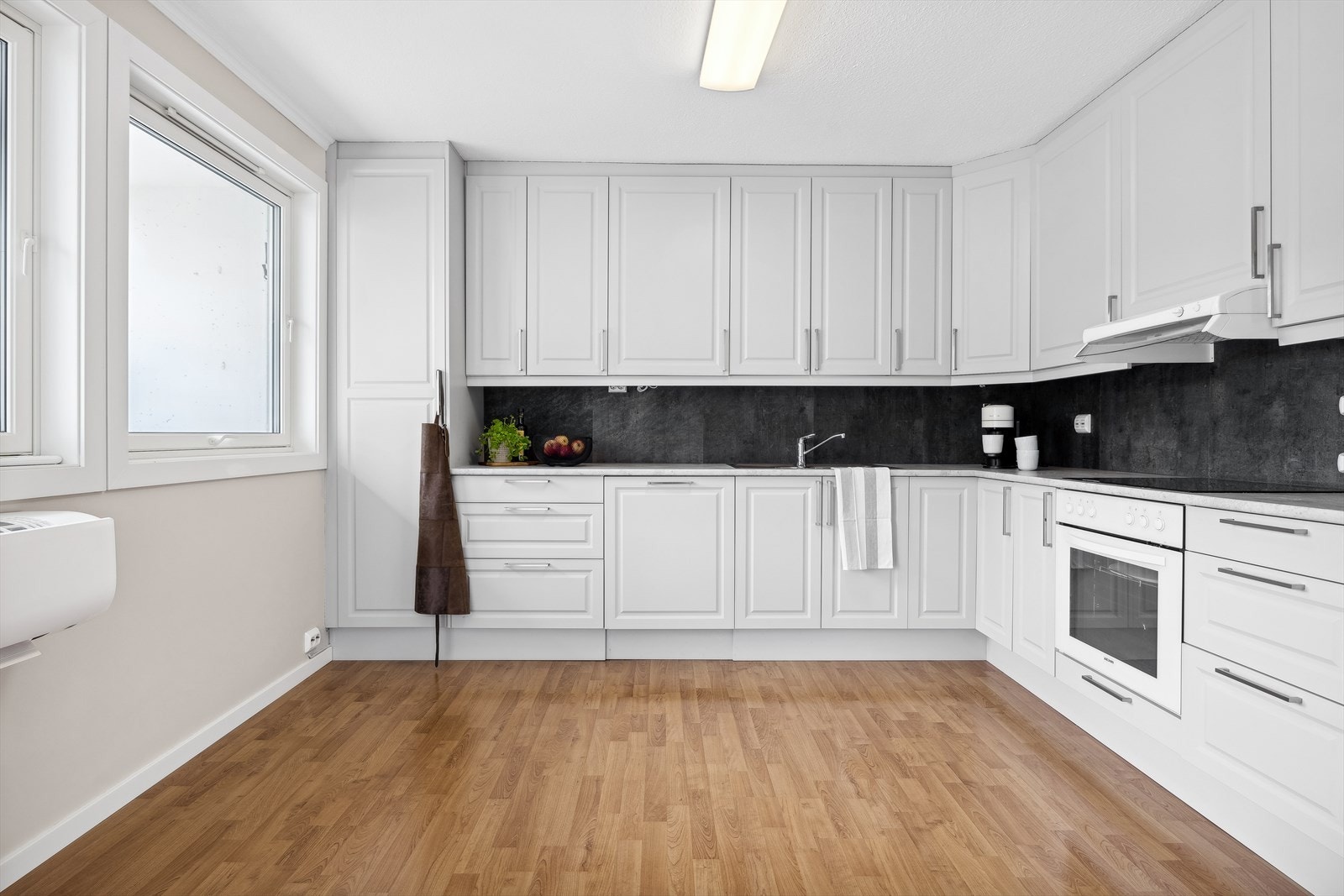 Pent kjøkken med hvite profilerte fronter og benkeplate med oppvaskkum. Galleribilde