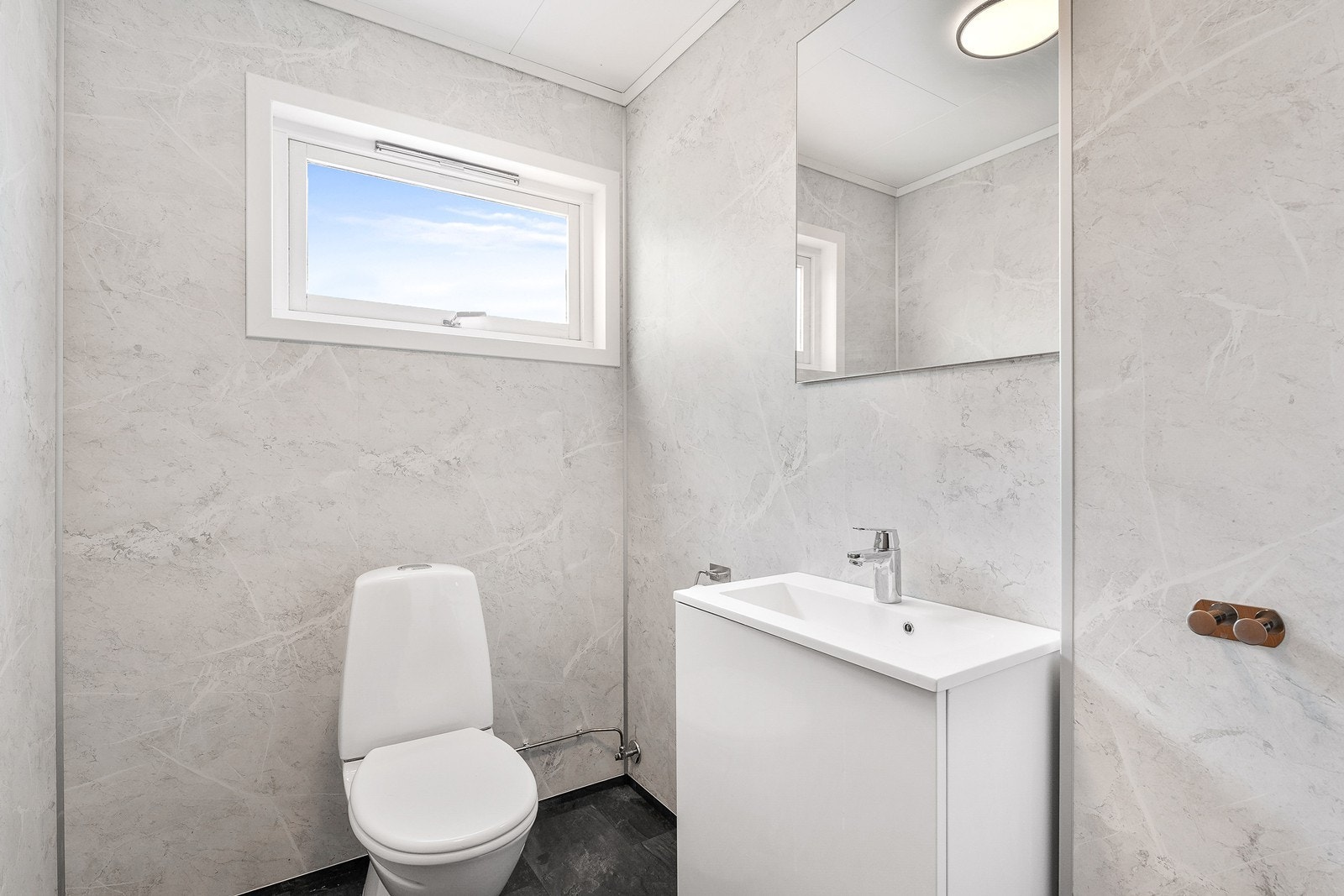 Toalettrom i etasjen har også baderomsplater på vegger og belegg på gulv. Innredet med toalett og servant med speil. Galleribilde